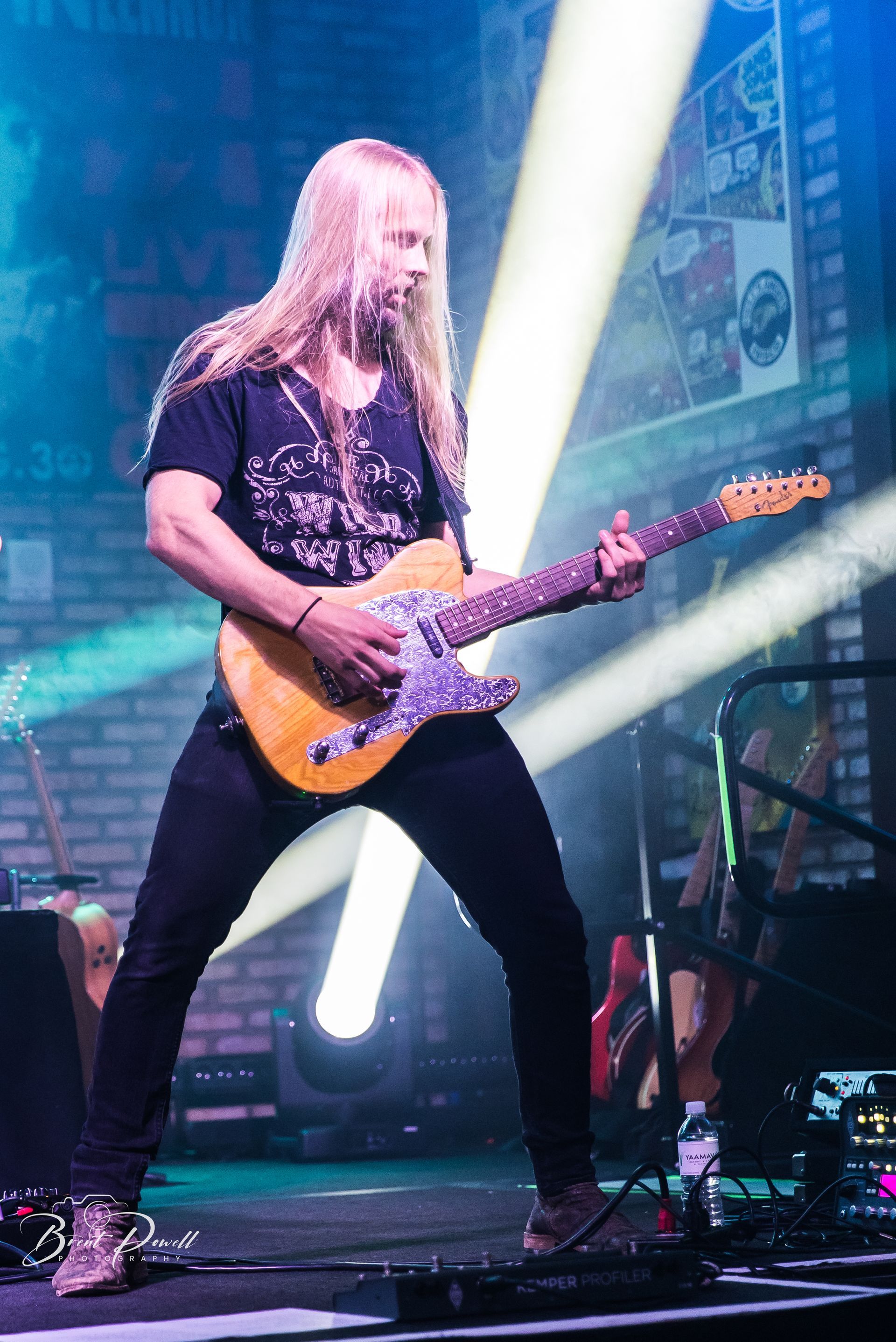 A man with long blonde hair is playing a guitar on a stage.