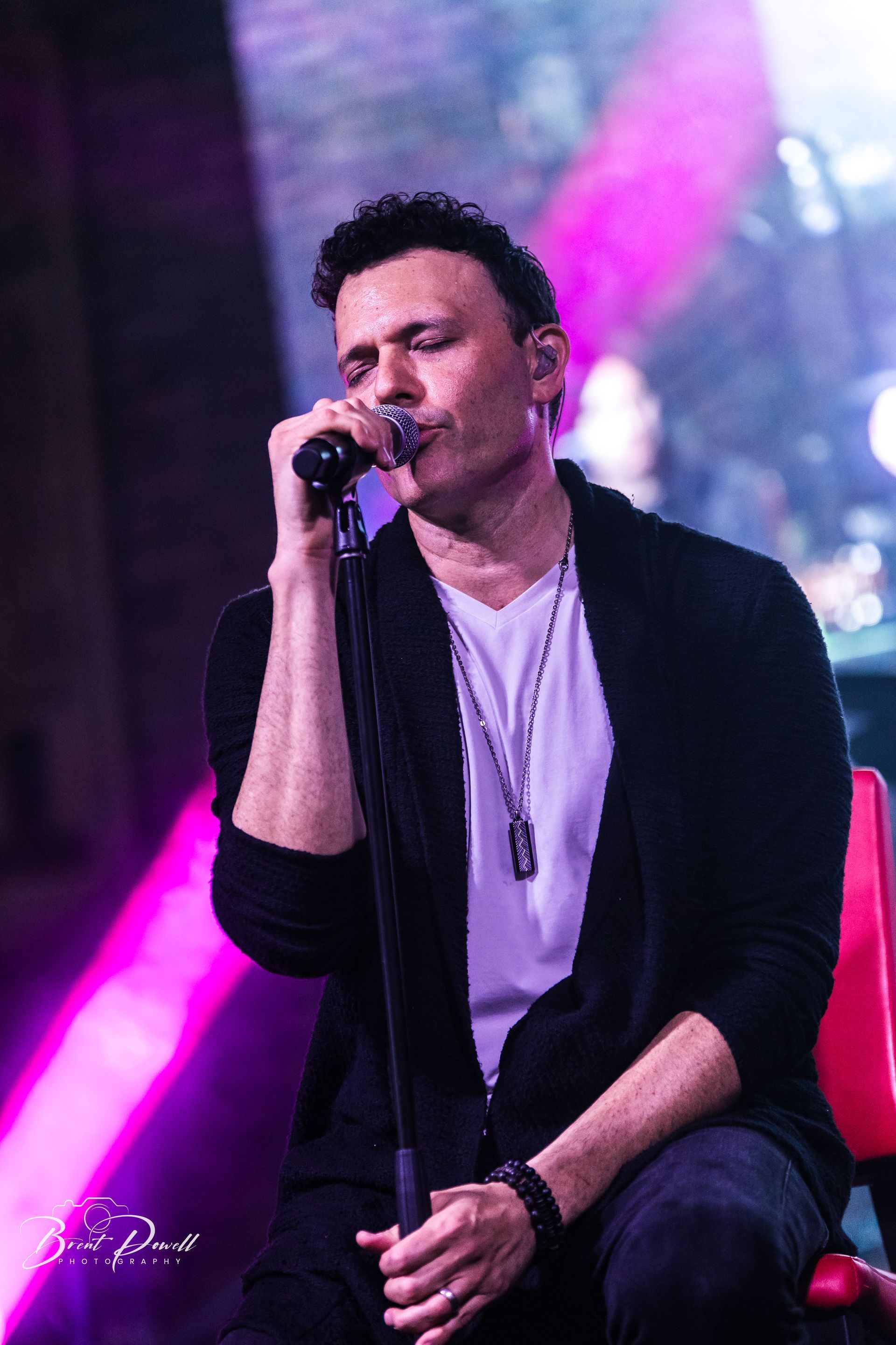 A man is singing into a microphone while sitting in a chair.