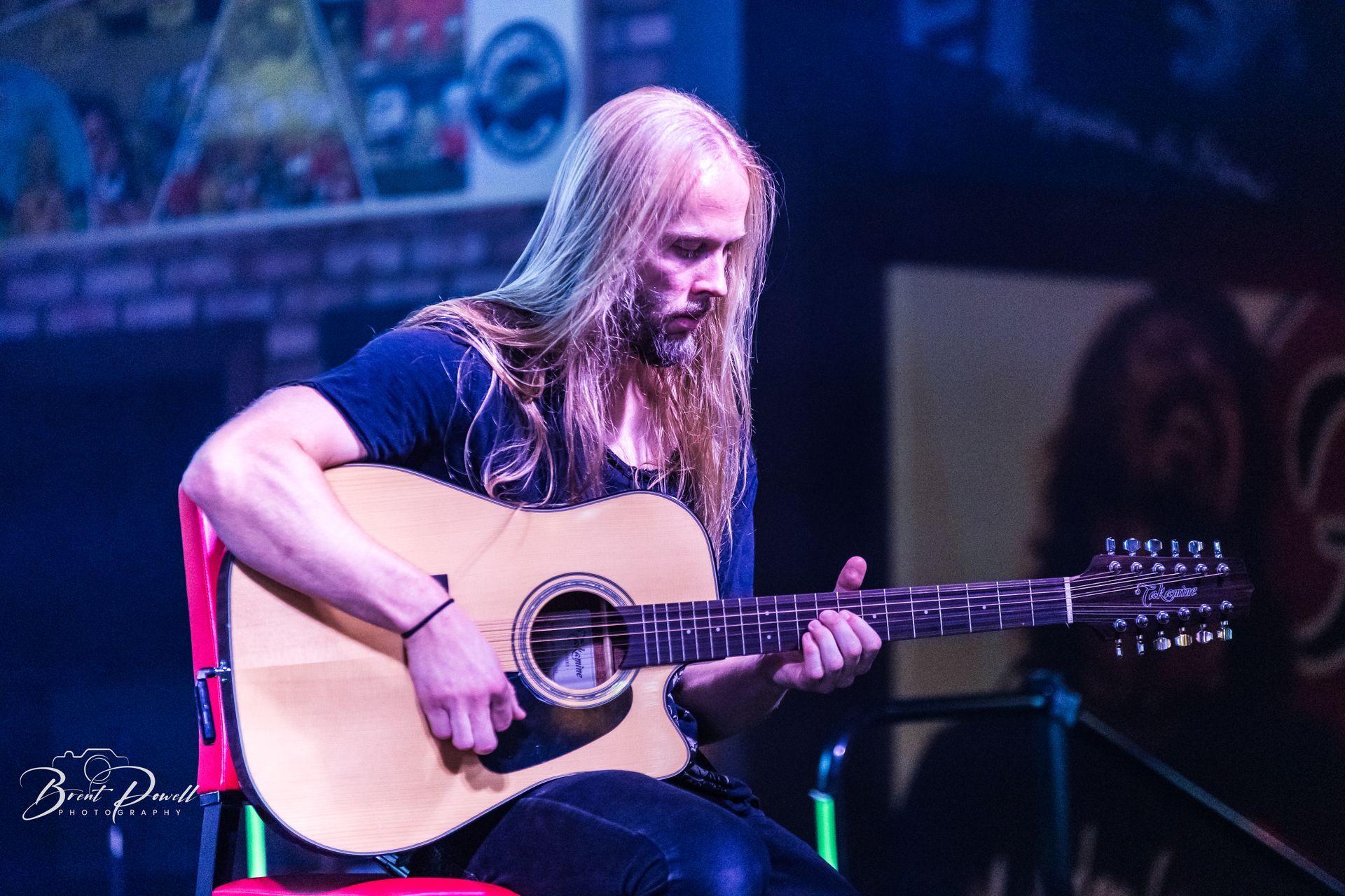 A man with long hair is playing an acoustic guitar on a stage.