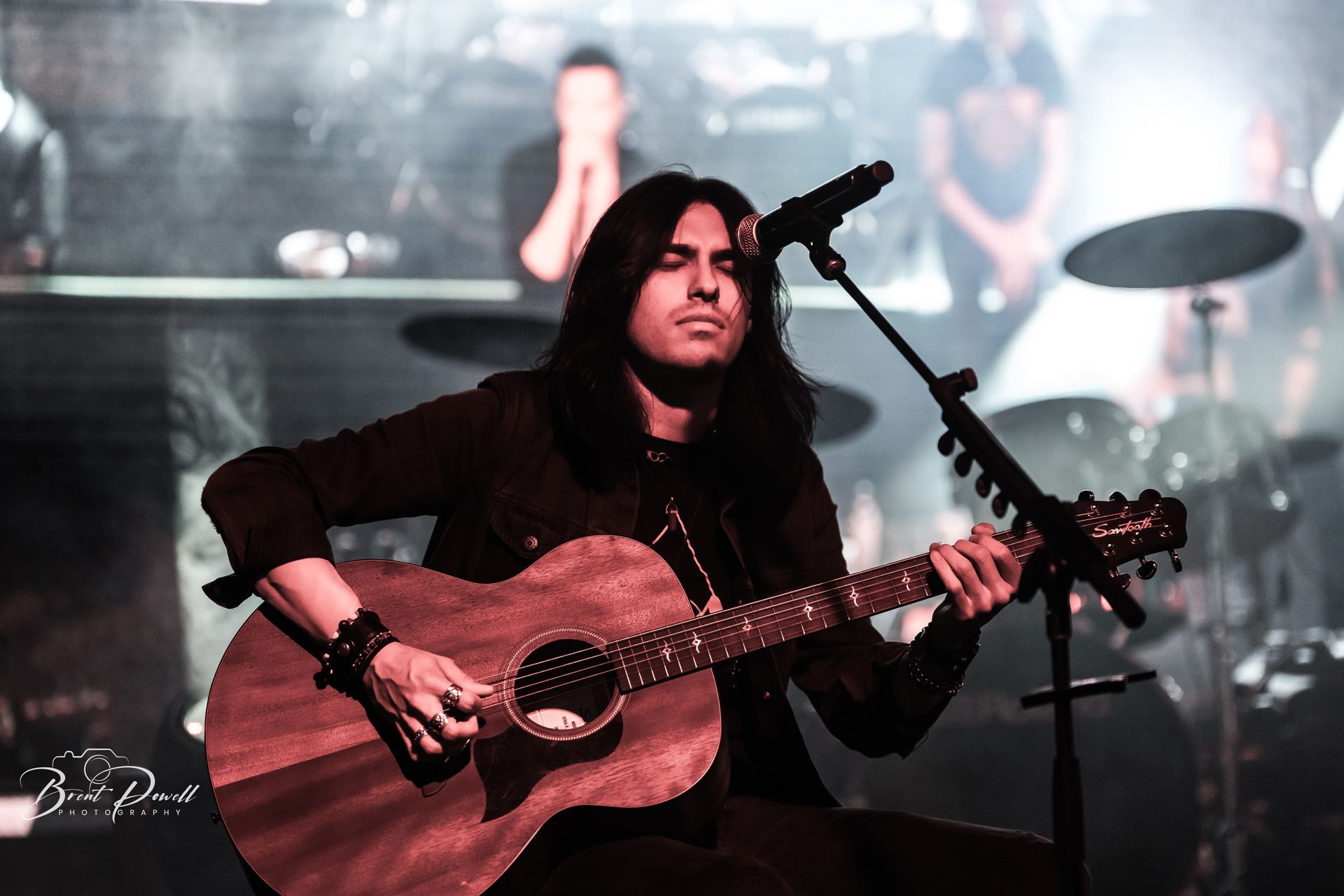 A man with long hair is playing a guitar and singing into a microphone