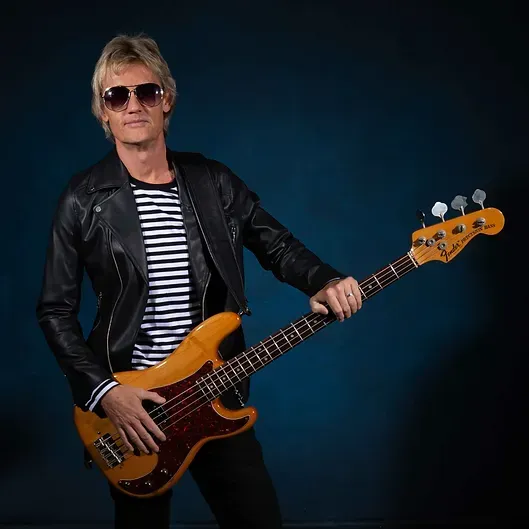 aaron samson in a leather jacket is holding a bass guitar.