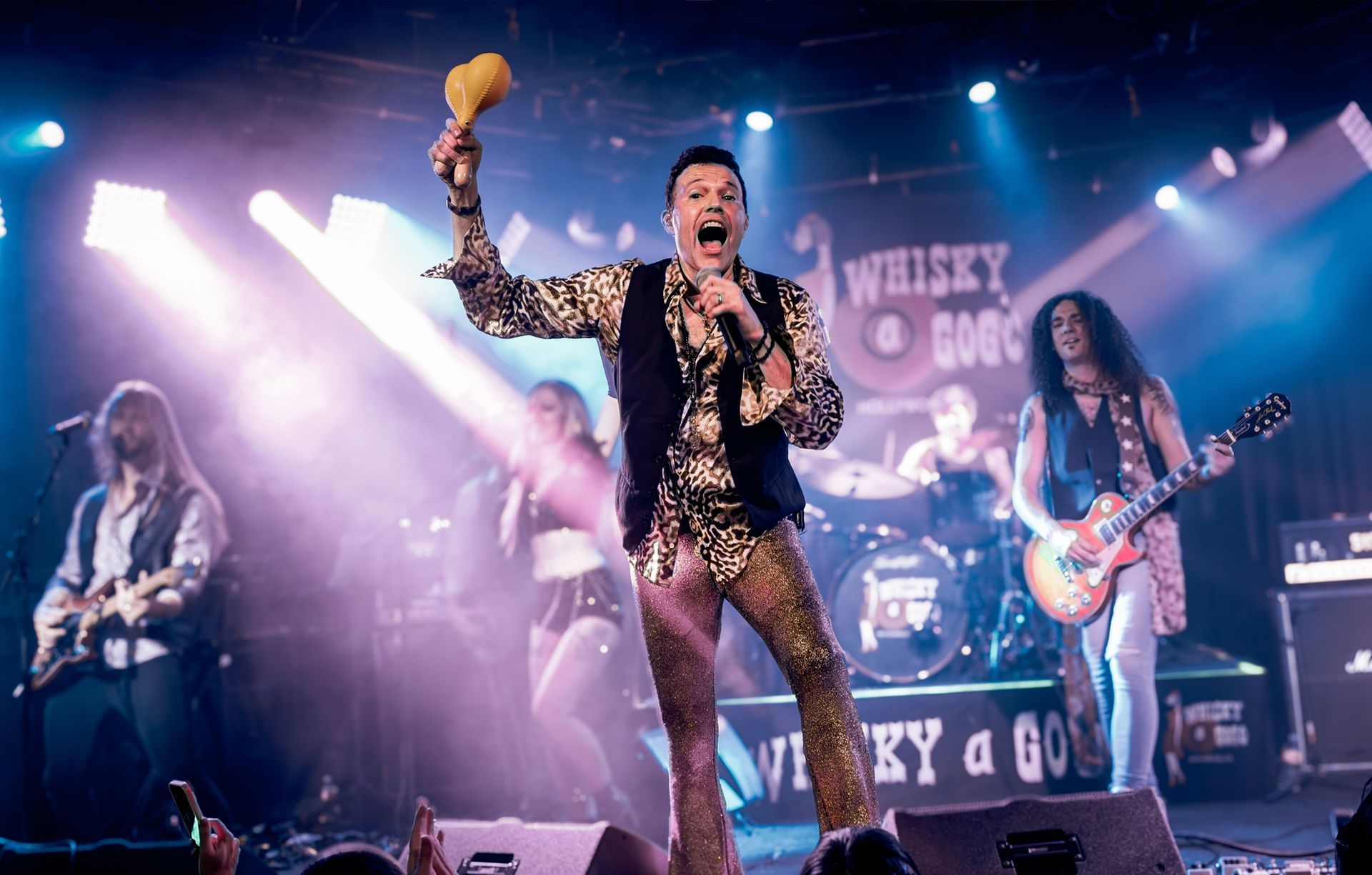 A man is singing into a microphone on a stage with a band behind him.