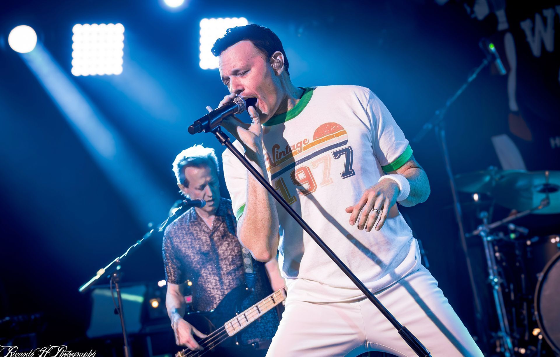A man is singing into a microphone while another man plays a guitar on stage.