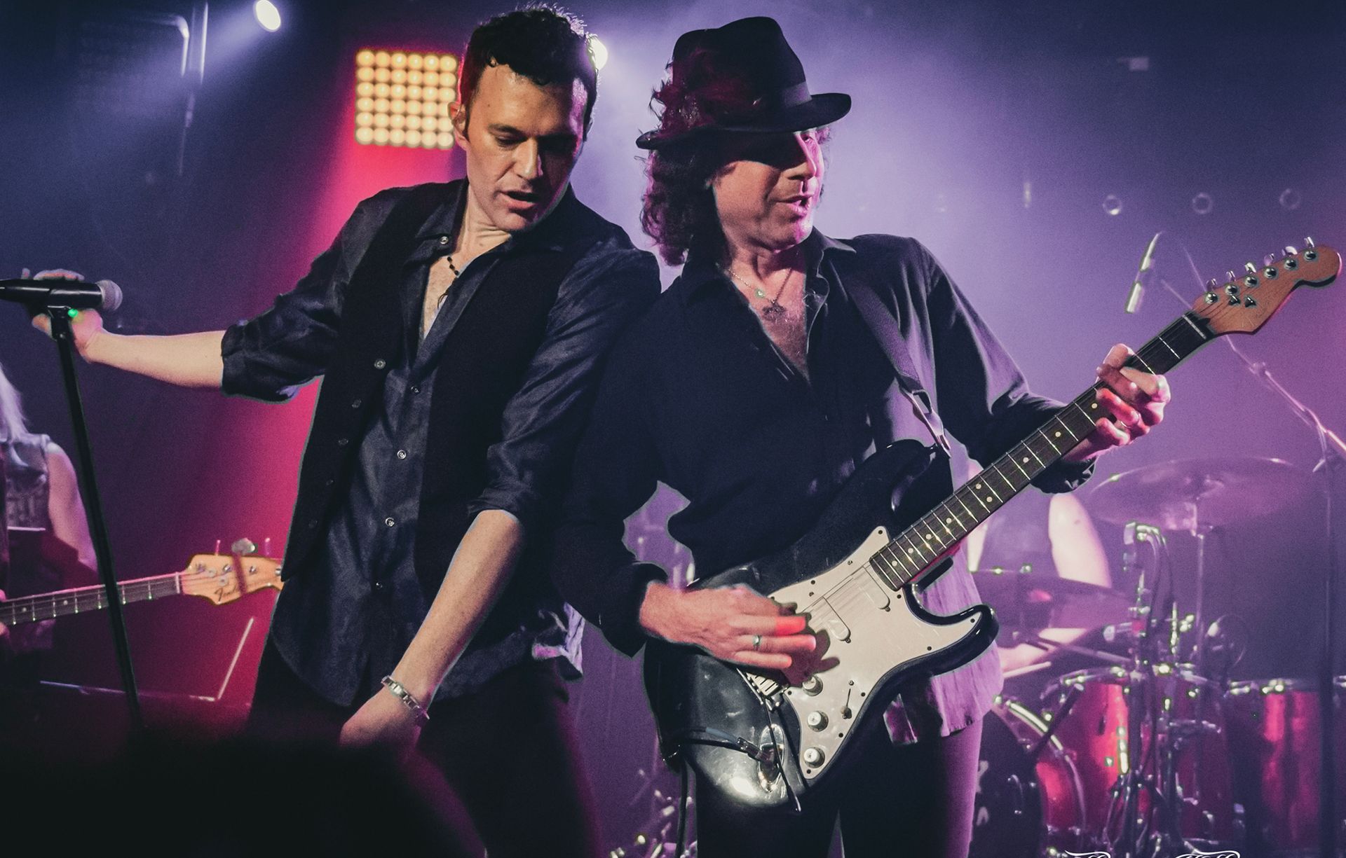 Two men are playing guitars and singing into microphones on a stage.