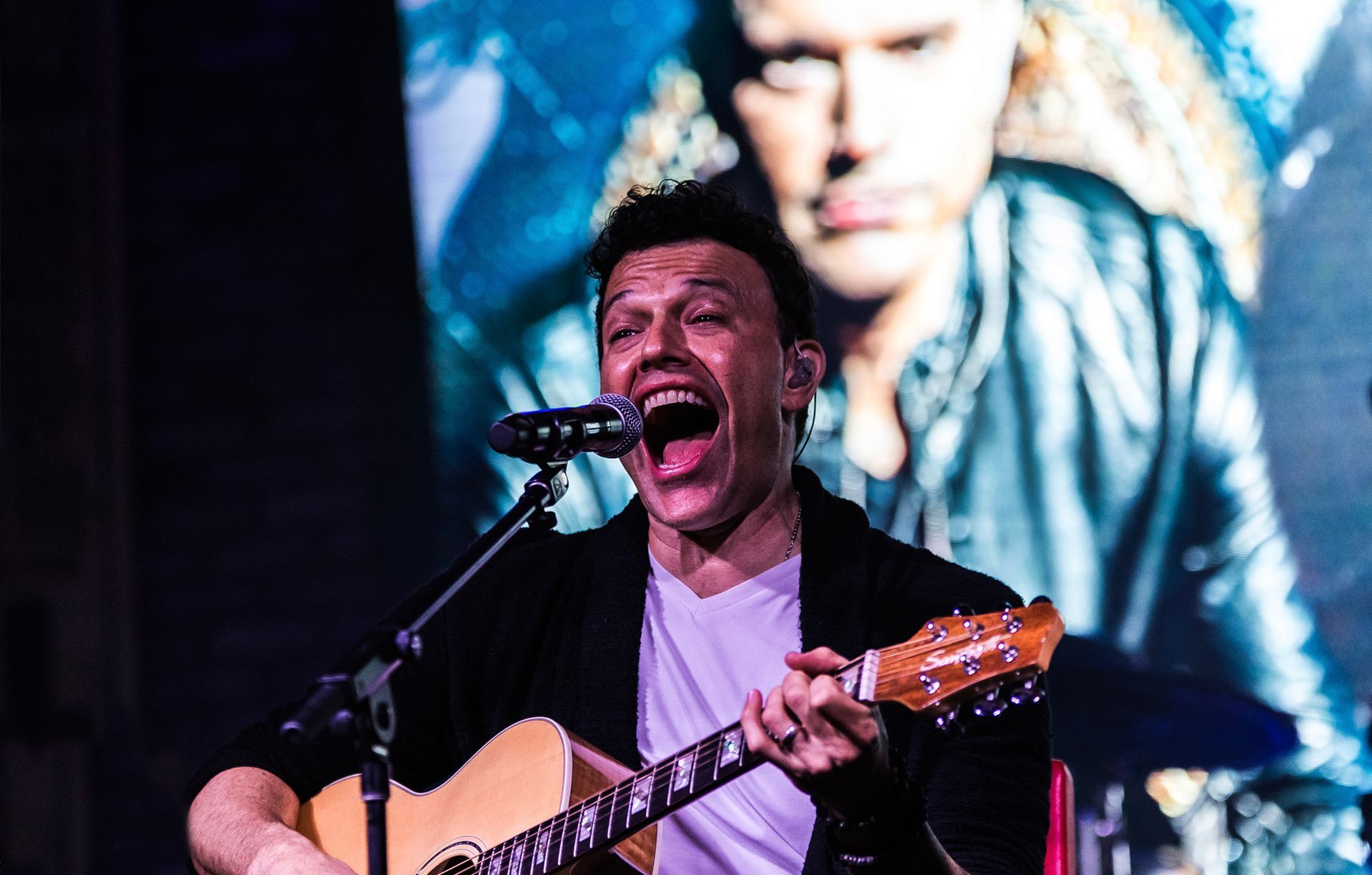 A man is singing into a microphone while playing a guitar.