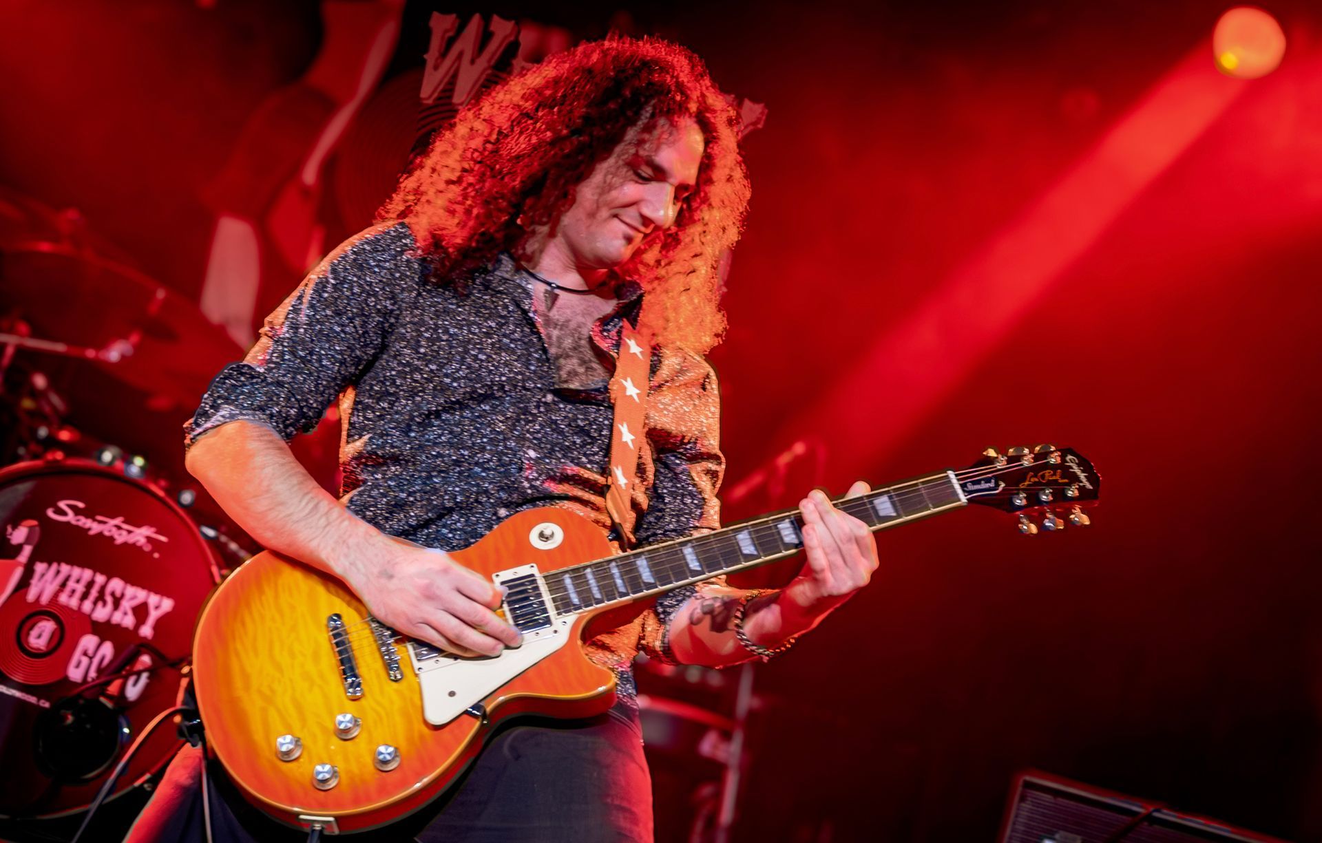 A man with long curly hair is playing a guitar on a stage.