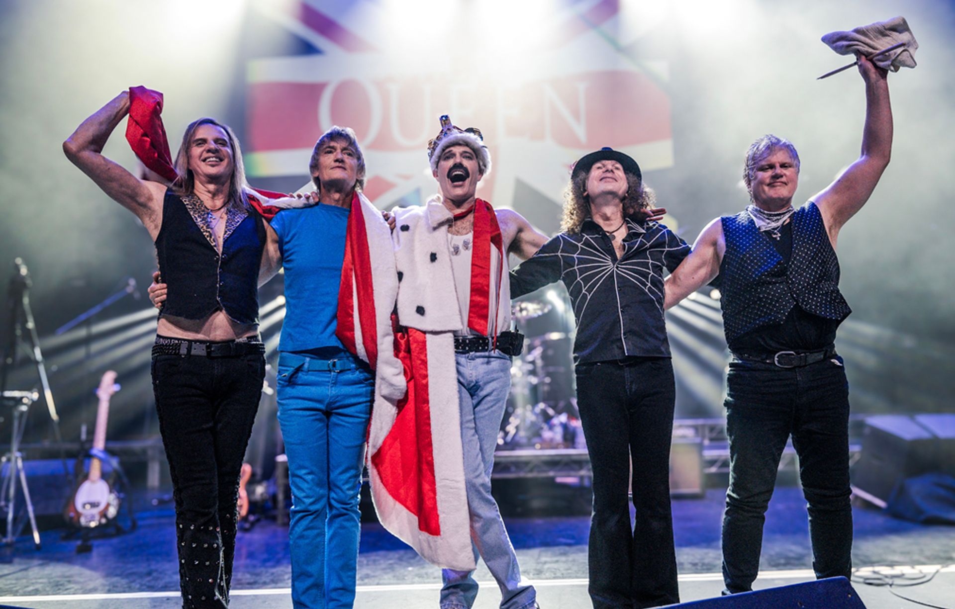 A group of men are standing on a stage in front of a sign that says queen
