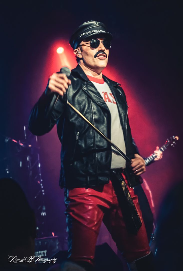 A man in a leather jacket is singing into a microphone while holding a guitar
