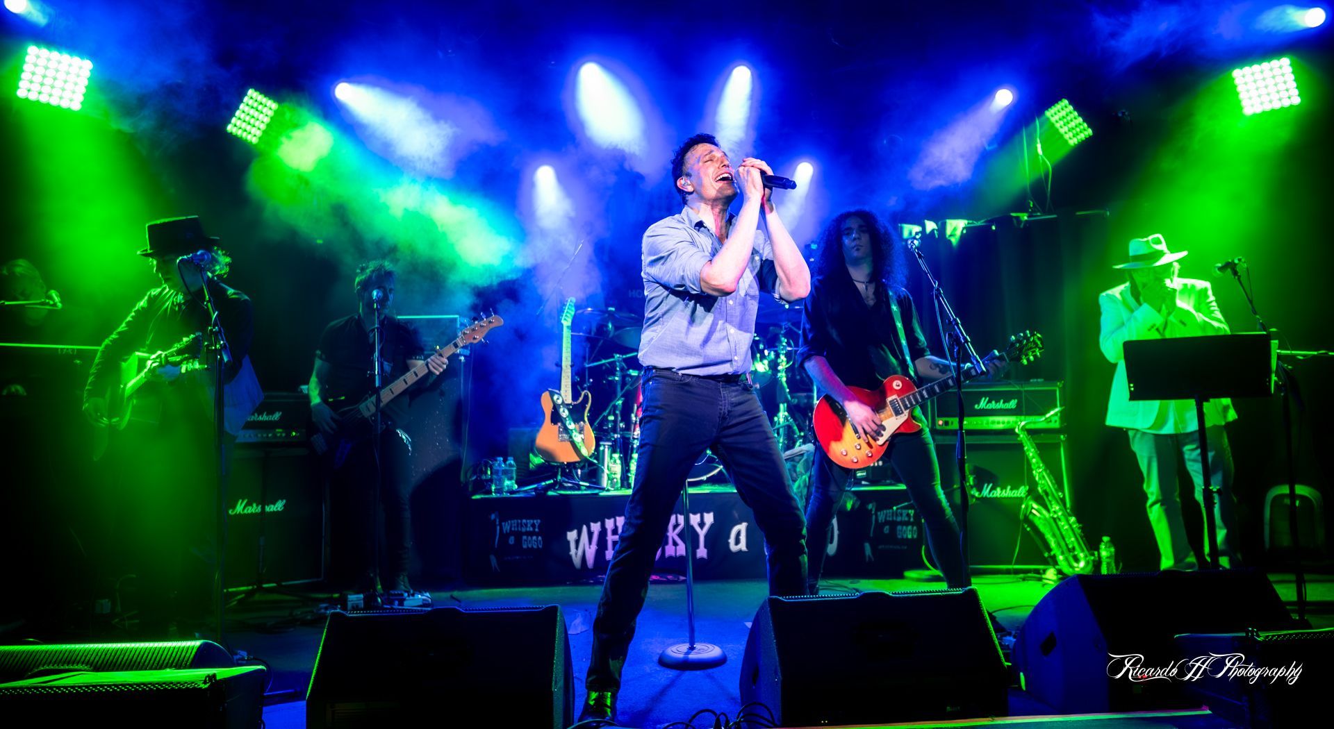 A man is singing into a microphone on a stage in front of a band.