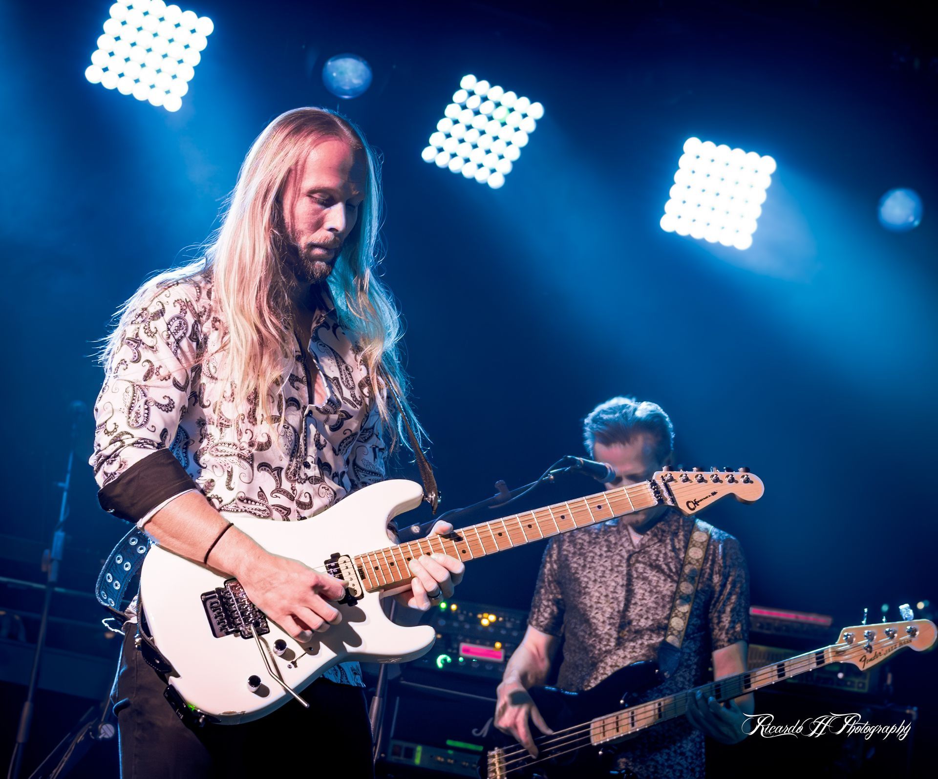 A man with long blonde hair is playing a guitar on stage
