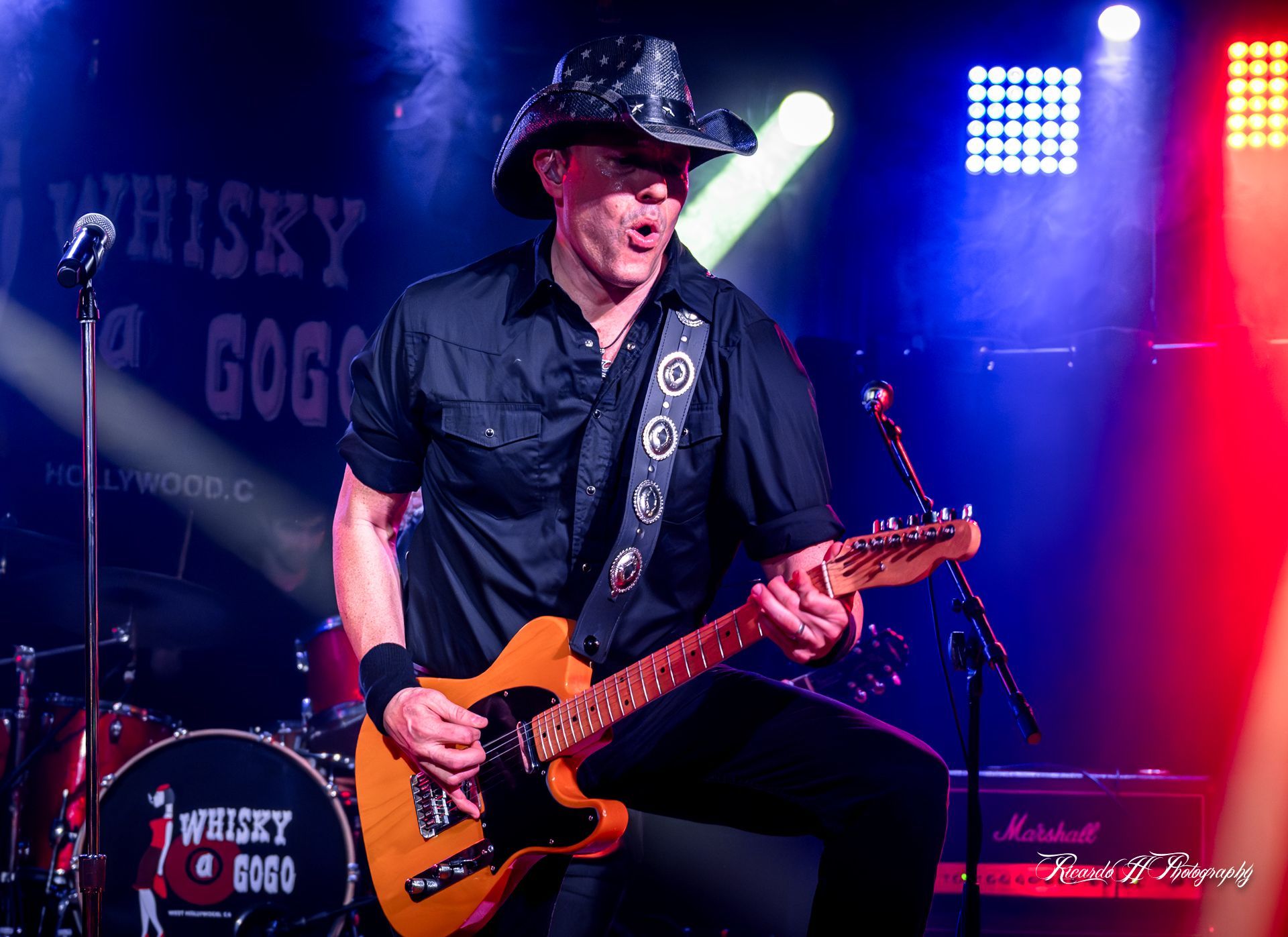A man in a cowboy hat is playing a guitar on a stage.