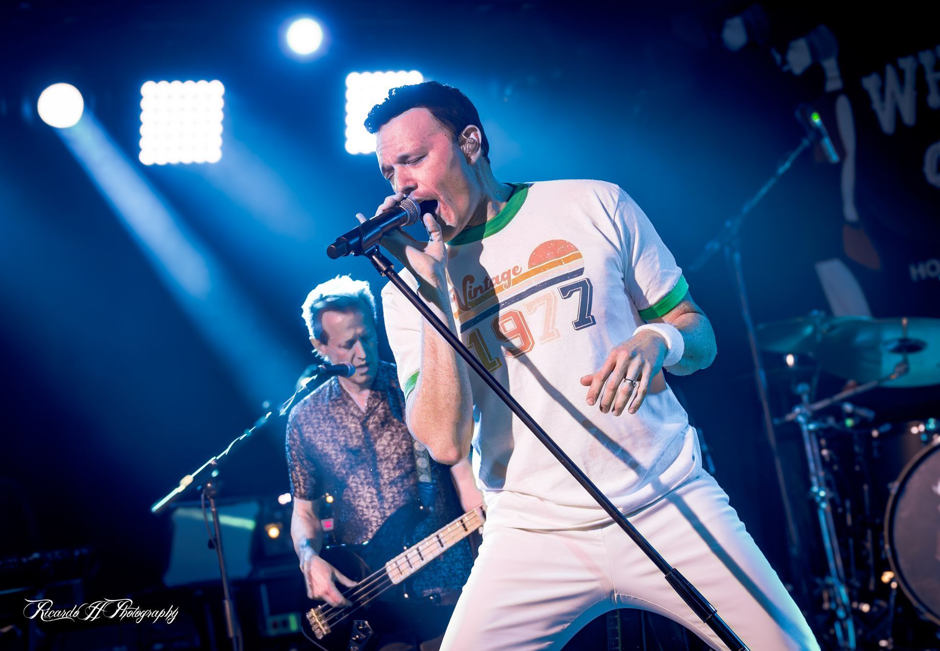 A man is singing into a microphone while another man plays a guitar on stage.