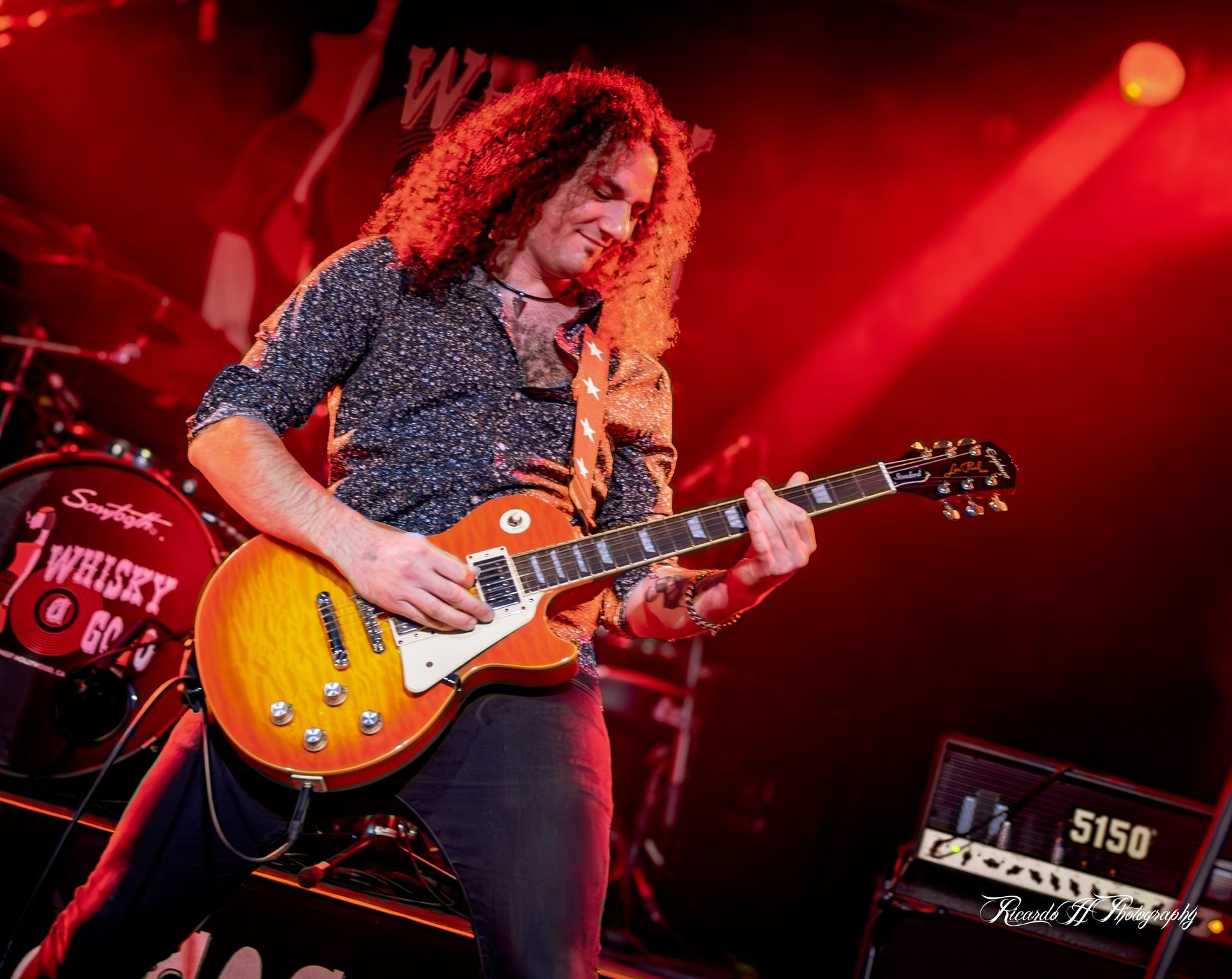 A man with curly hair is playing a guitar on a stage.