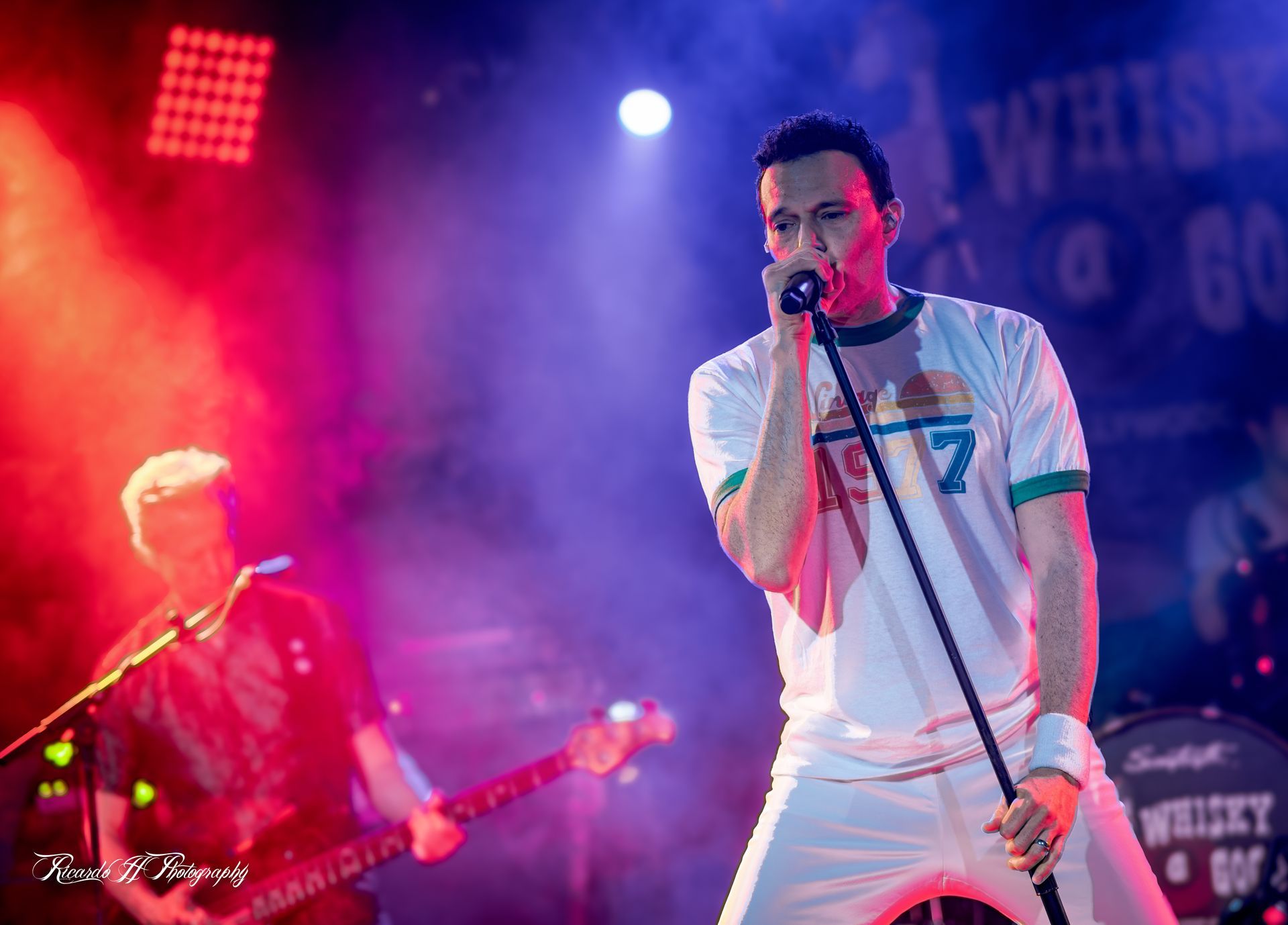 A man is singing into a microphone on a stage while another man plays a guitar.