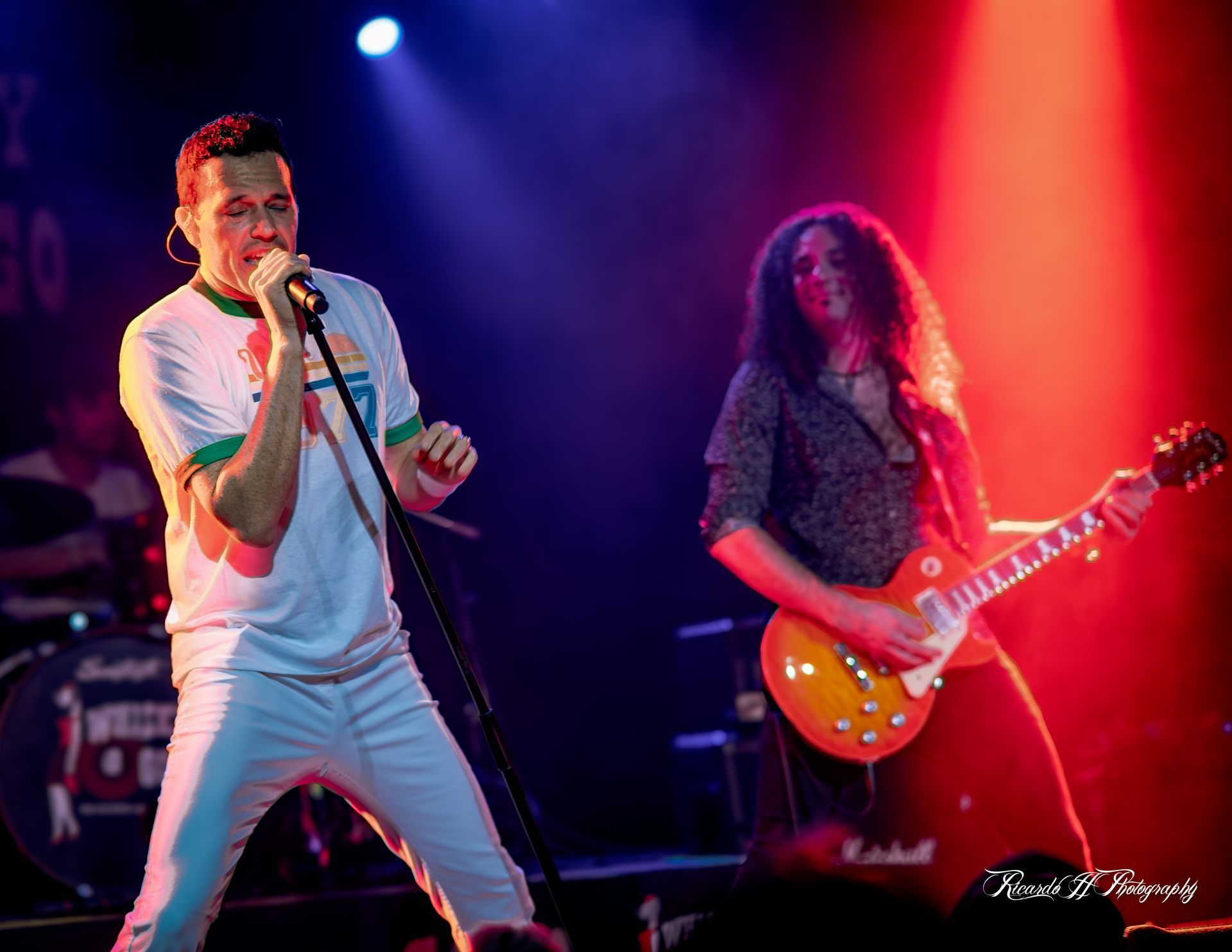 A man is singing into a microphone while a woman plays a guitar on stage.
