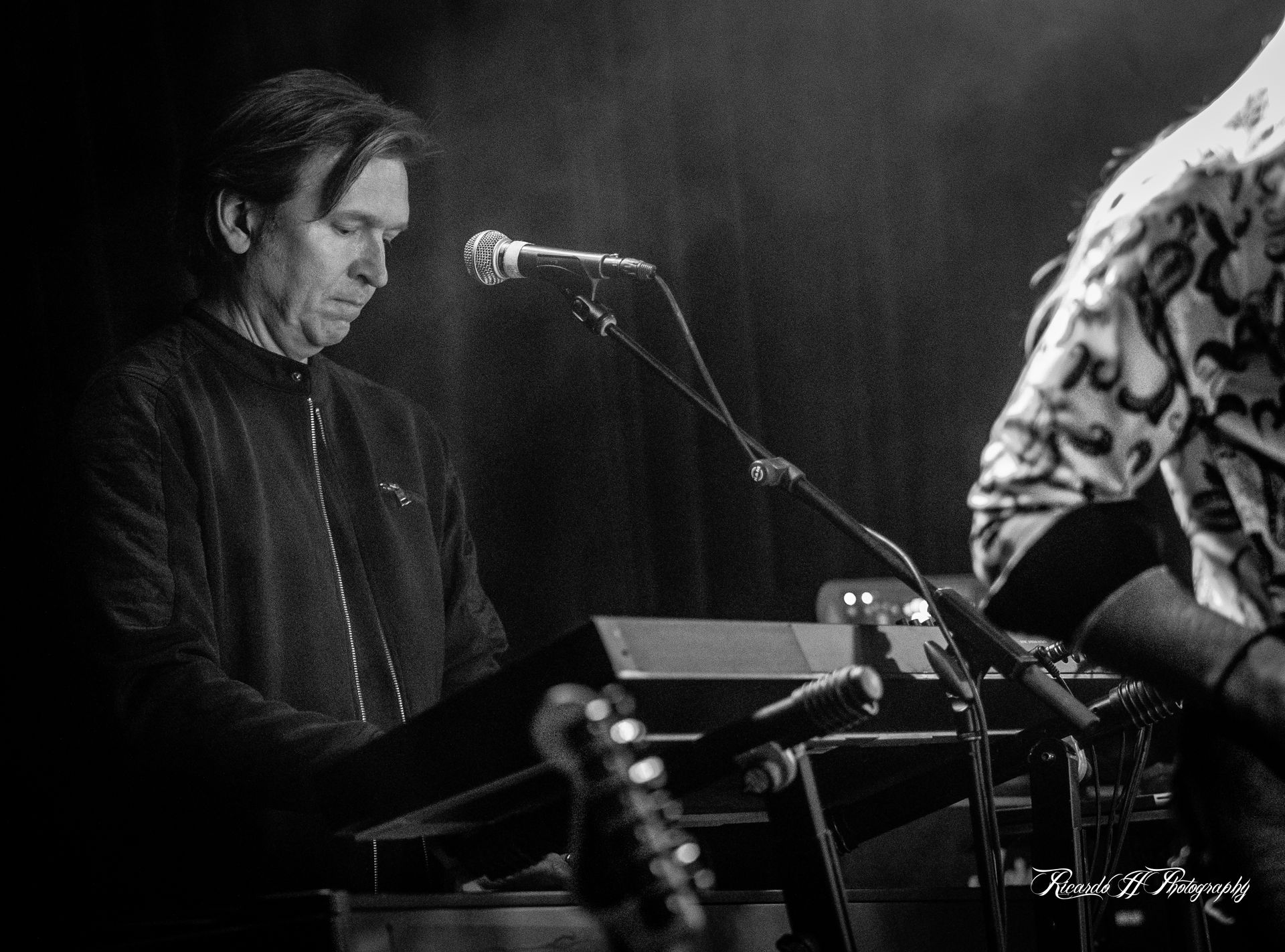A man is playing a keyboard in front of a microphone in a black and white photo.