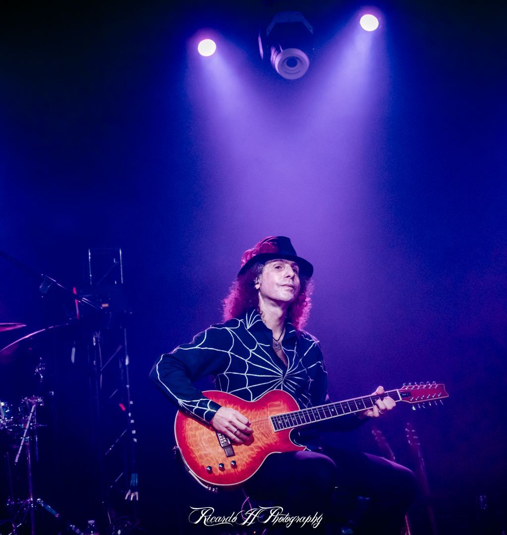 A man is playing a guitar on a stage with purple lights behind him.