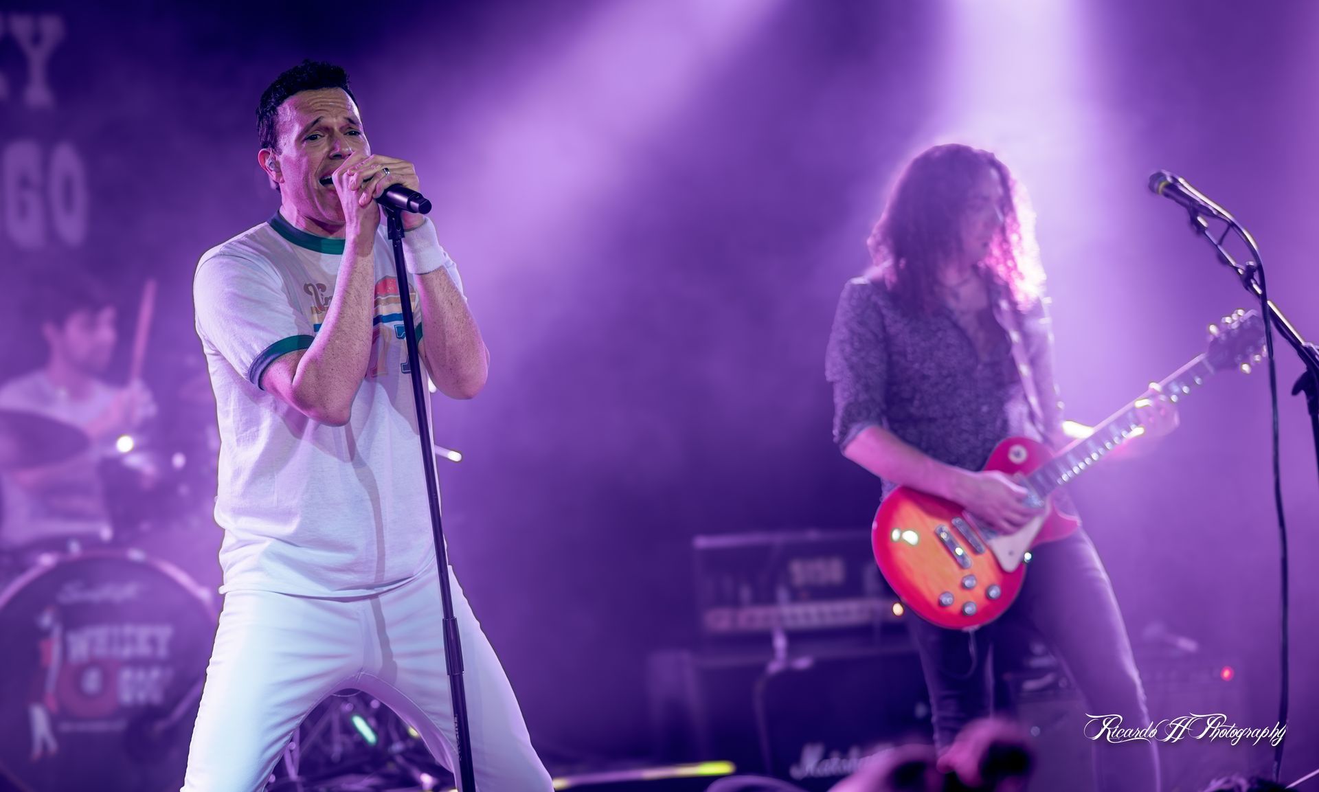 A man is singing into a microphone while another man plays a guitar on stage.