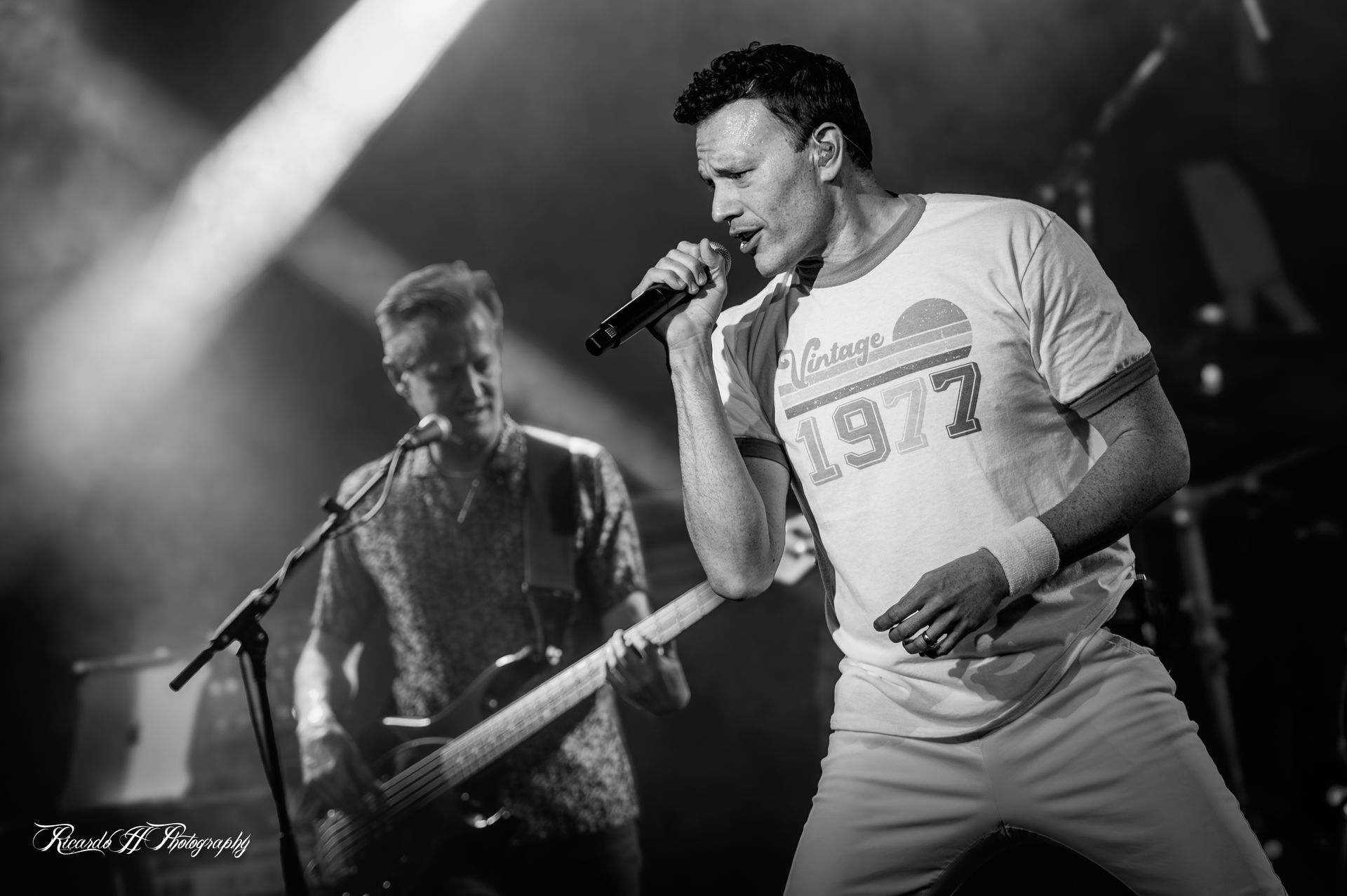 A man is singing into a microphone while another man plays a guitar on stage.
