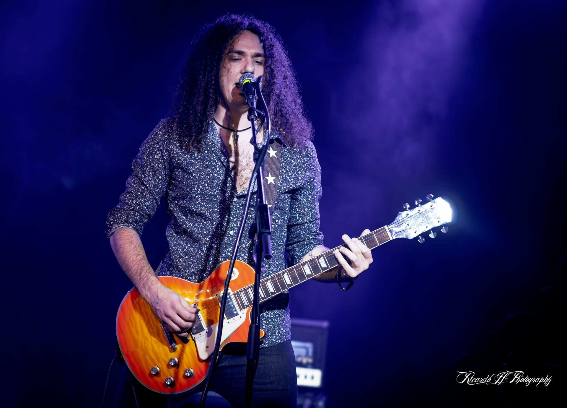 A man with long hair is playing a guitar and singing into a microphone on a stage.