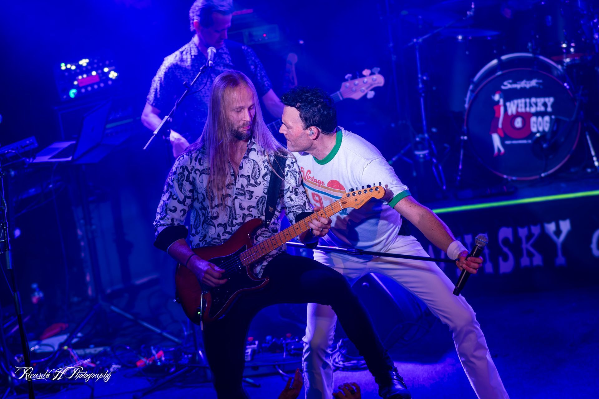 A man is playing a guitar on stage while another man sings into a microphone.