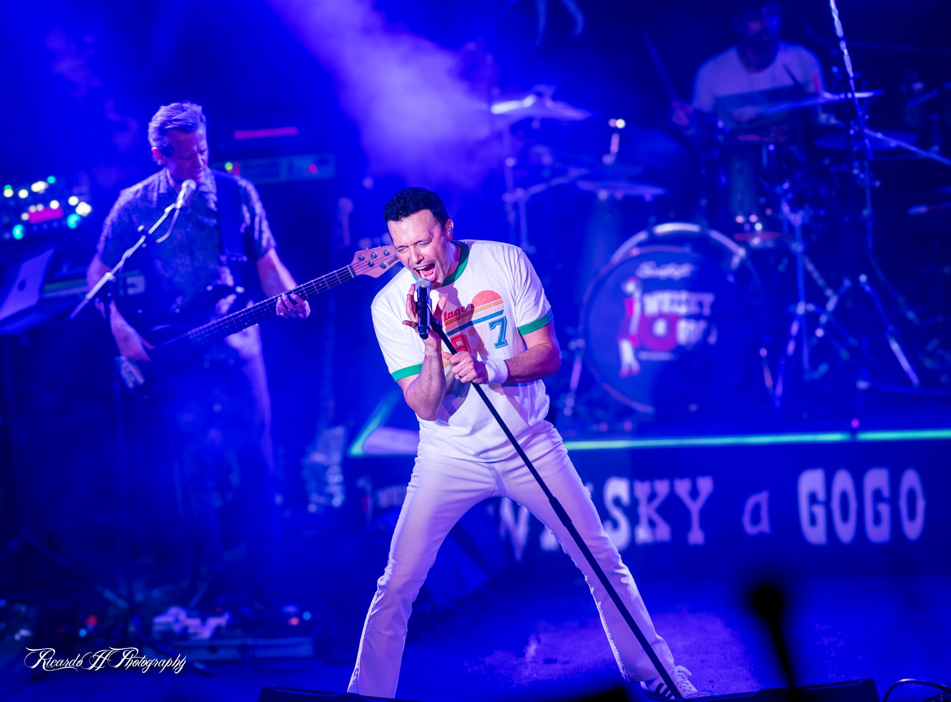 A man is singing into a microphone on a stage with a band behind him.