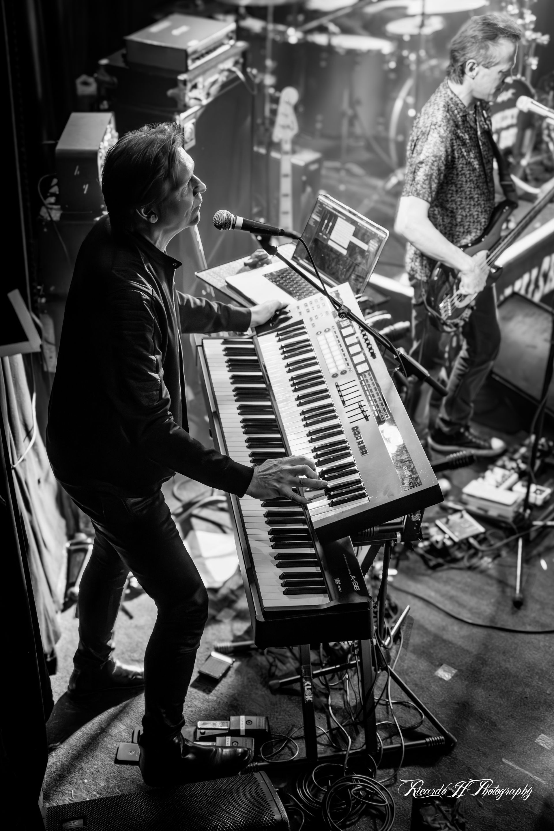 A man is playing a keyboard on stage in a black and white photo.