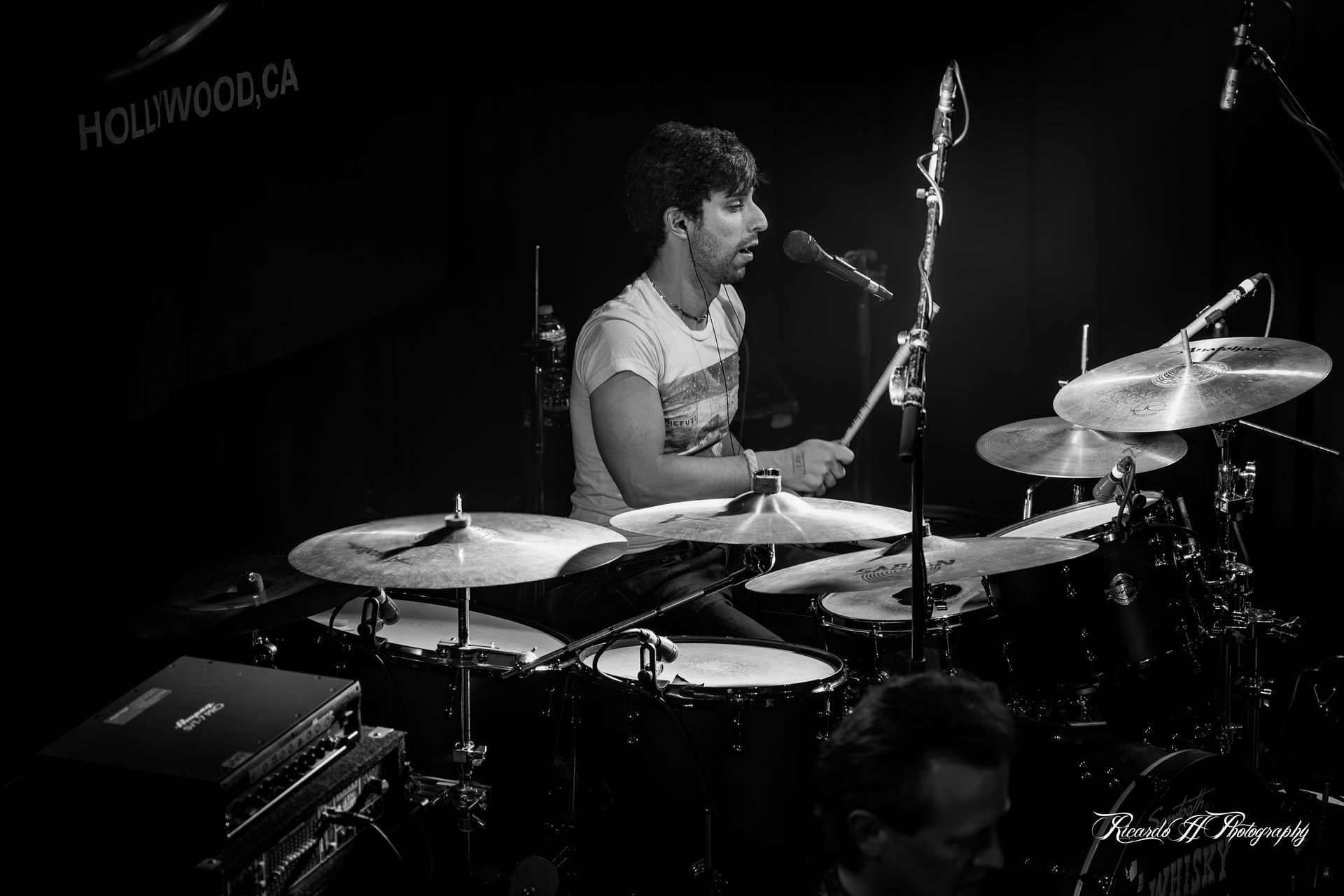 A man is playing drums on a stage in a black and white photo.