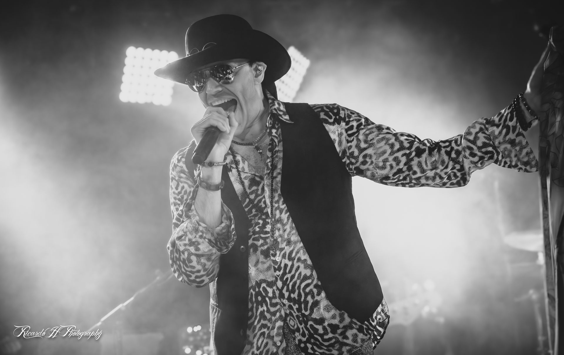 A man is singing into a microphone on a stage in a black and white photo.