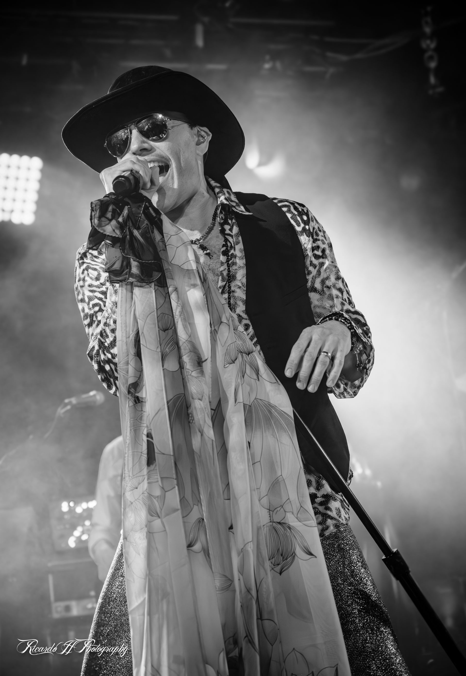 A man is singing into a microphone on a stage in a black and white photo.