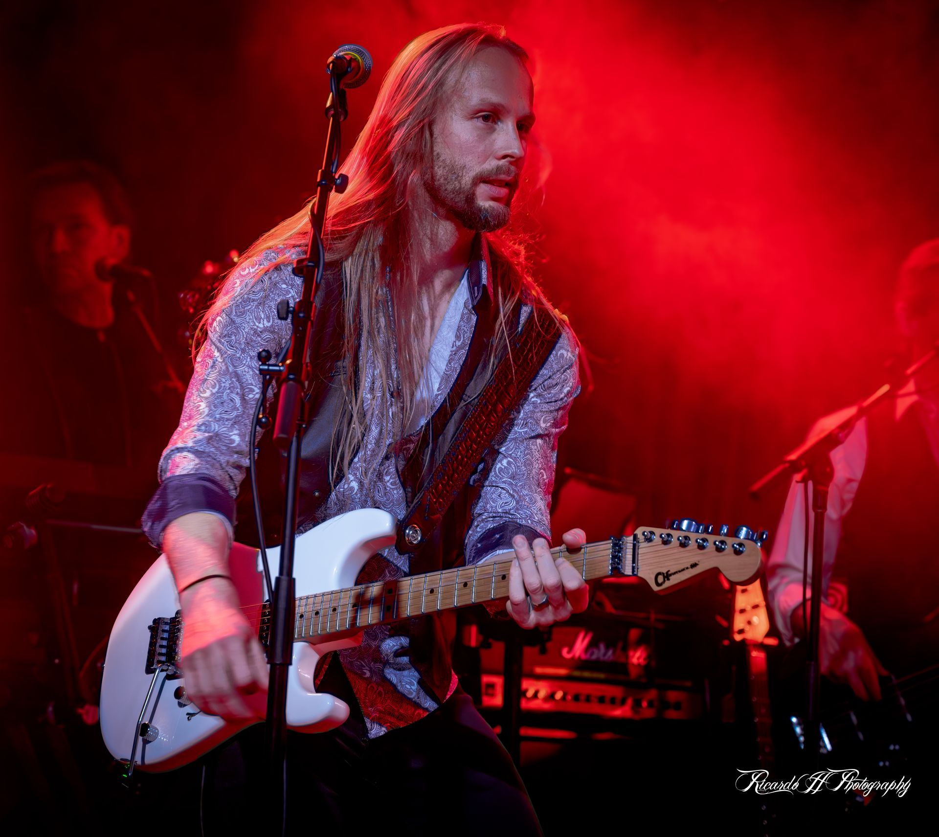 A man with long hair is playing a guitar and singing into a microphone