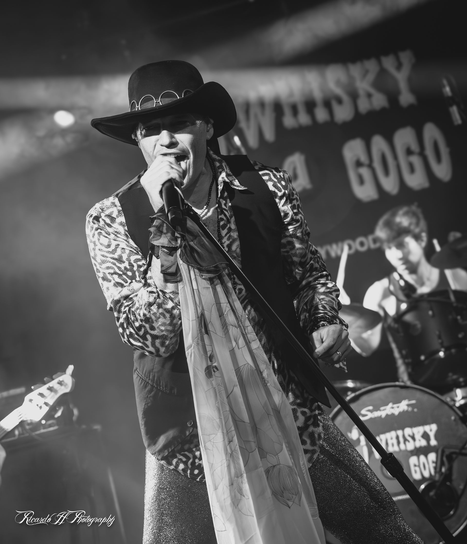A man singing into a microphone in front of a sign that says whisky gogo