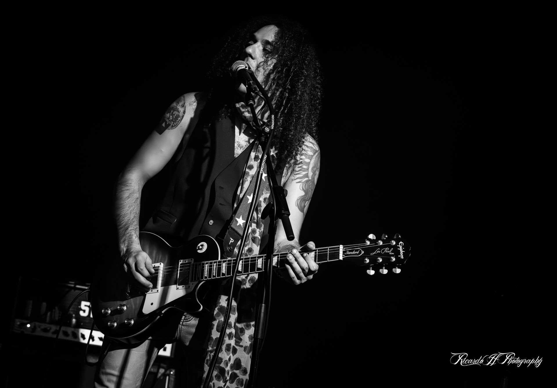 A man with long hair is playing a guitar and singing into a microphone.