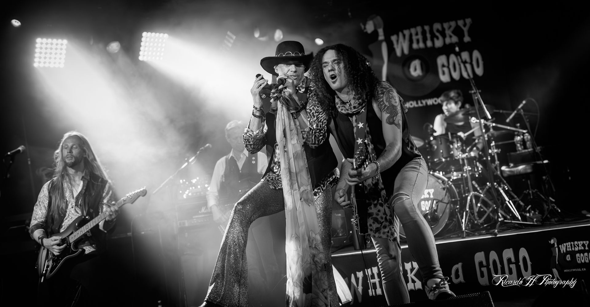 A black and white photo of a rock band on stage.