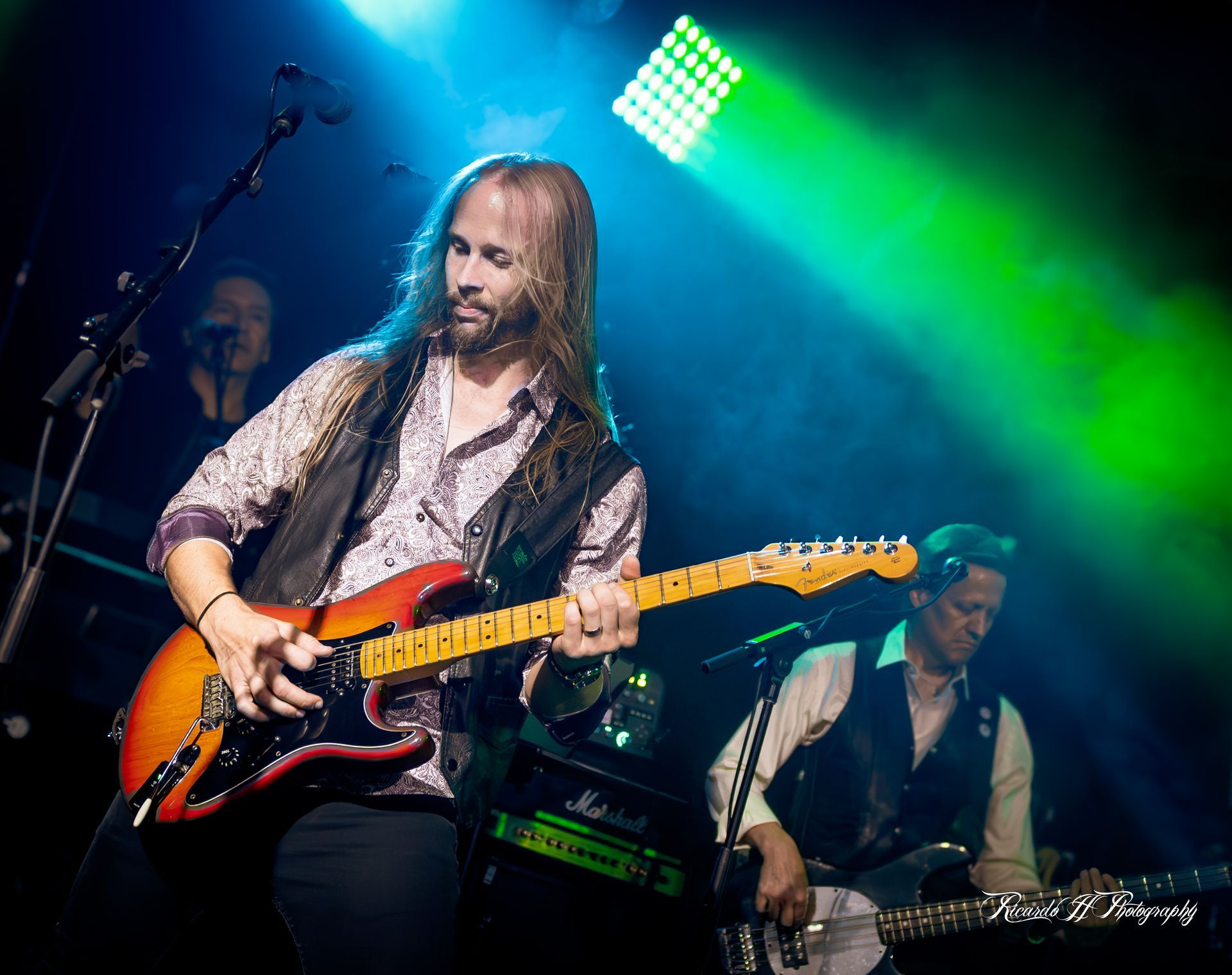 A man with long hair is playing a guitar on a stage.