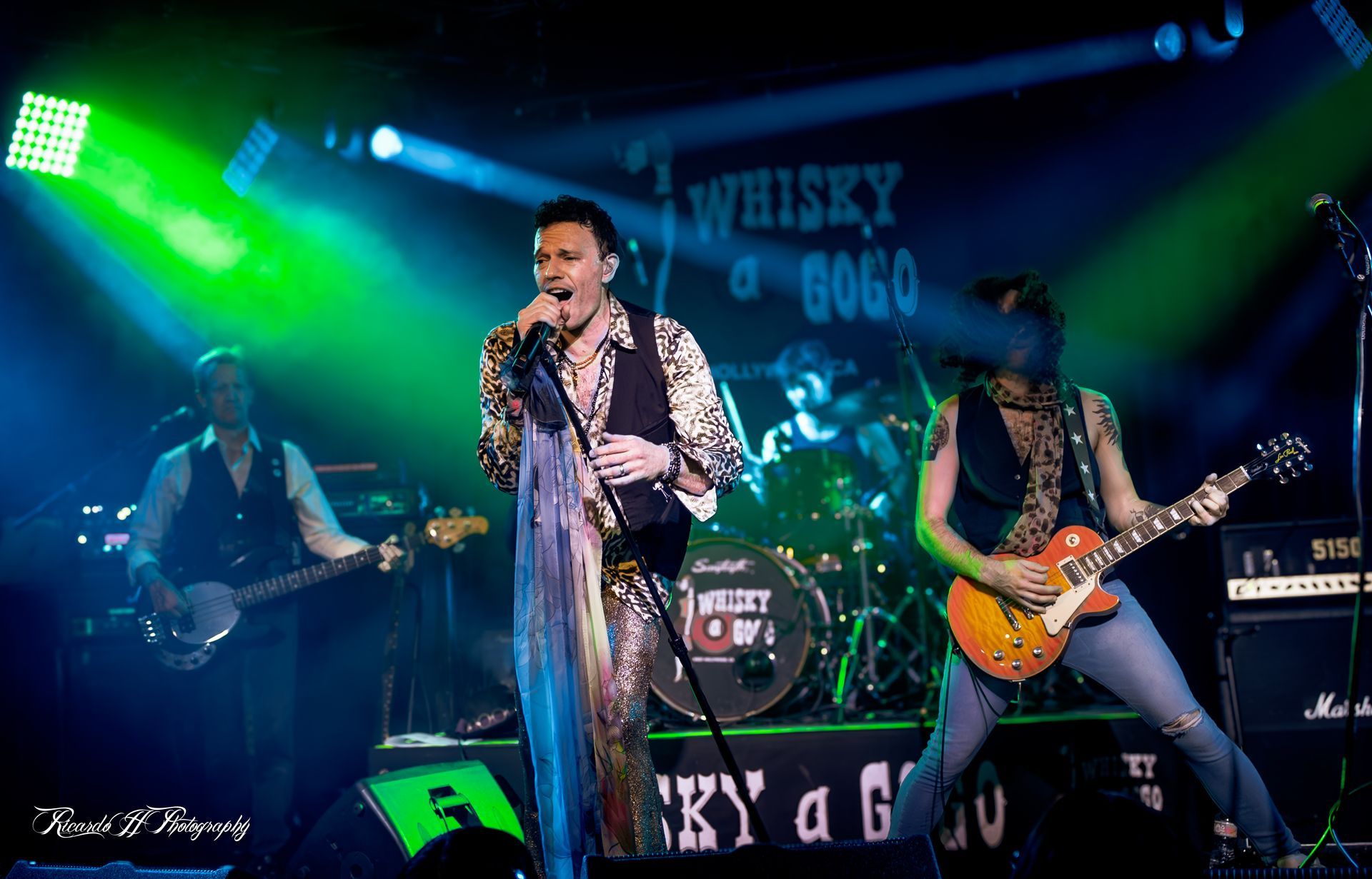 A man is singing into a microphone while two men play guitars on stage.