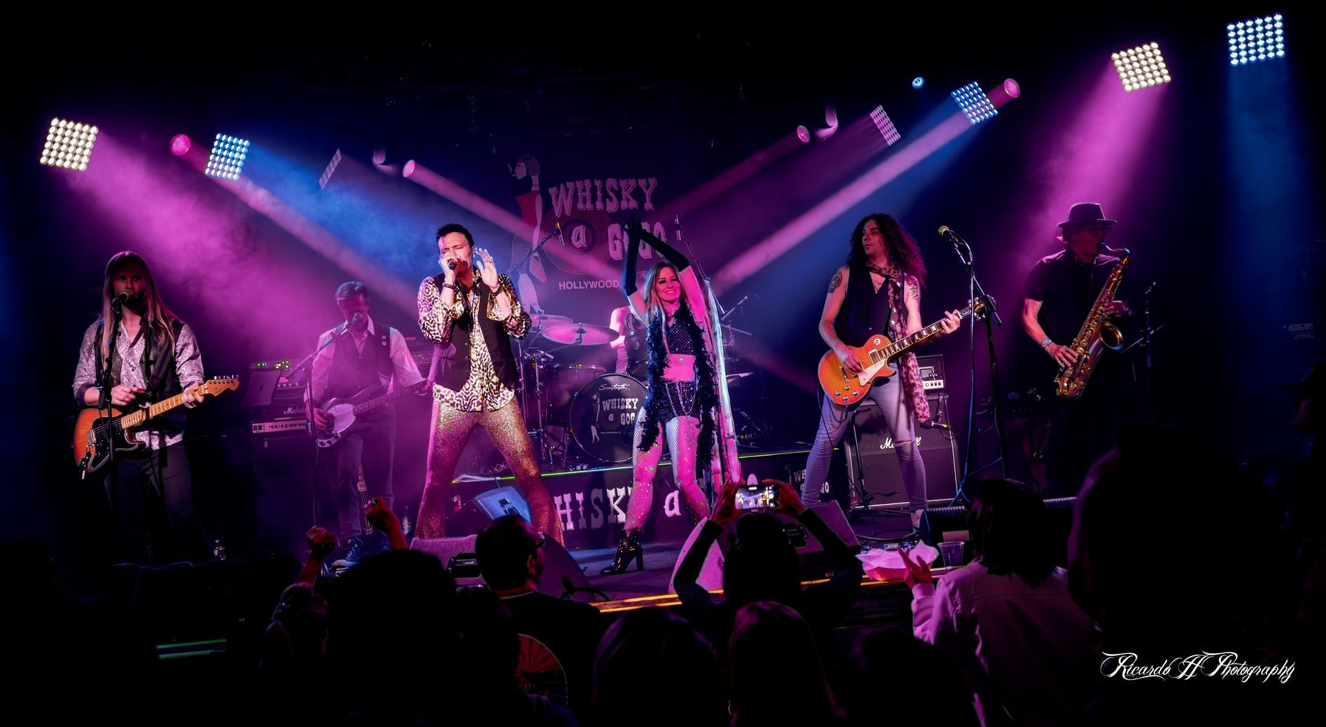 A group of people playing instruments on a stage with purple lights