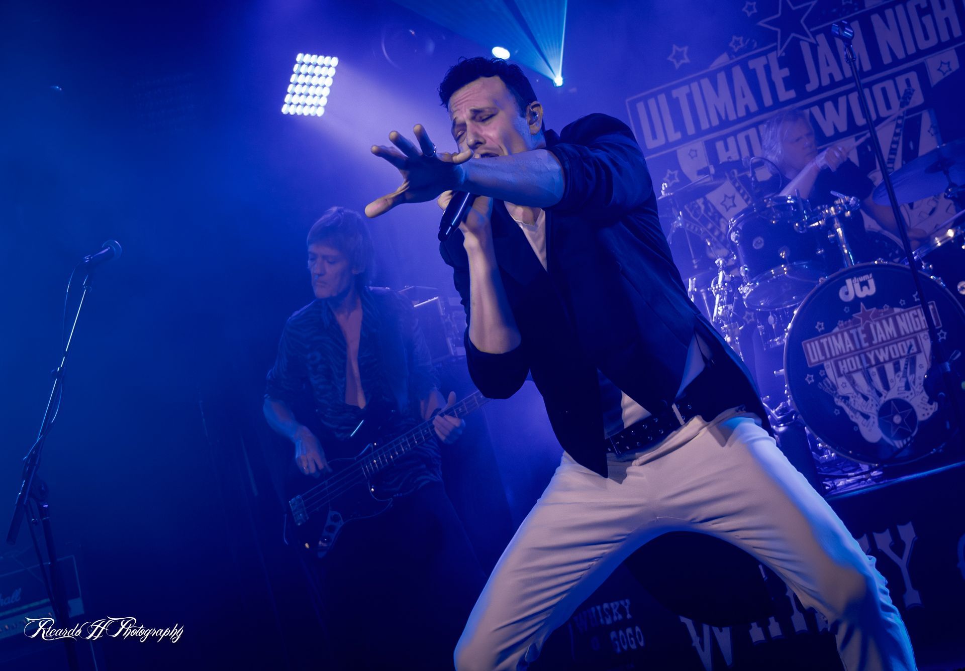 A man is singing into a microphone on a stage in front of a drum set.