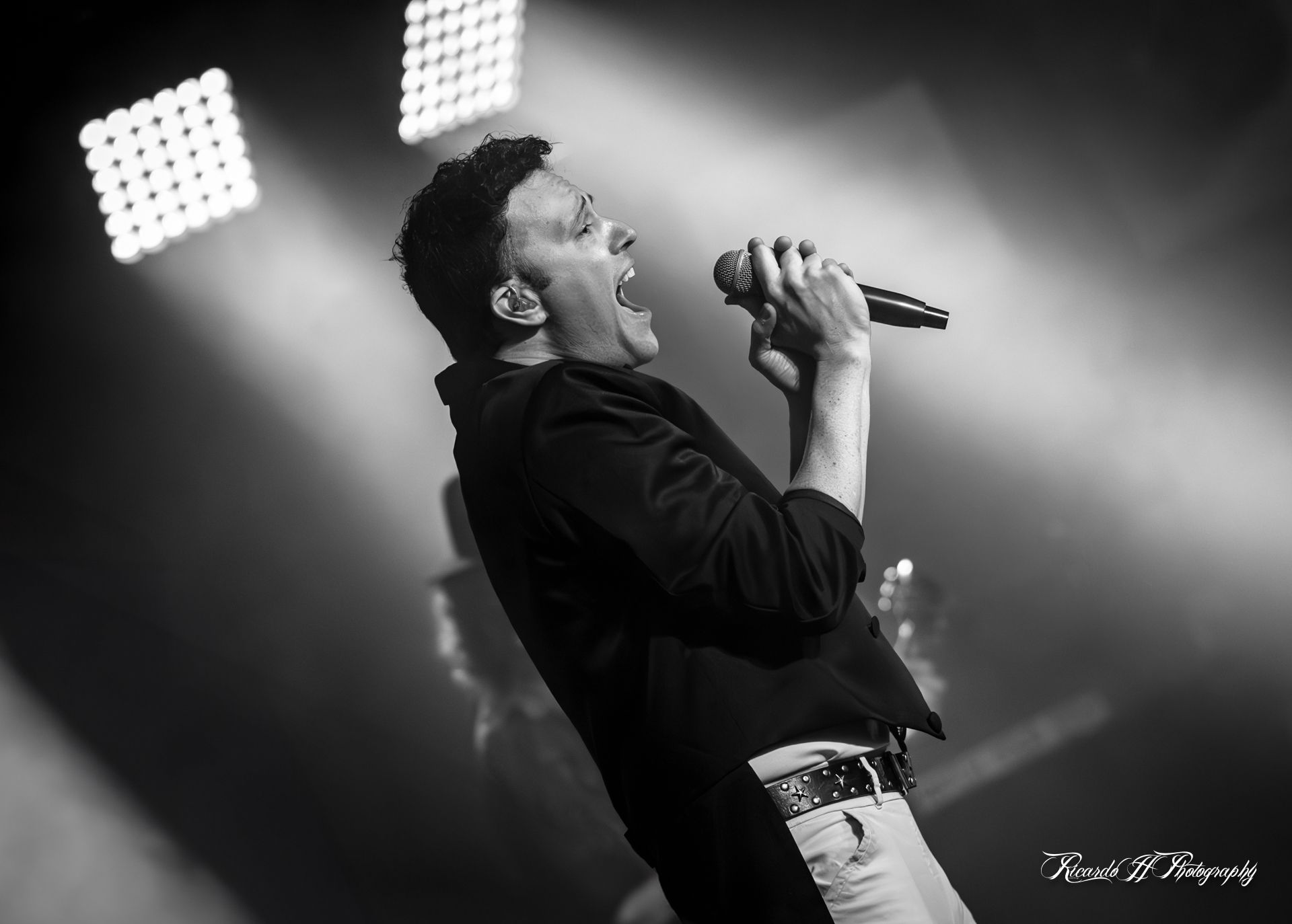 A man is singing into a microphone on a stage in a black and white photo.