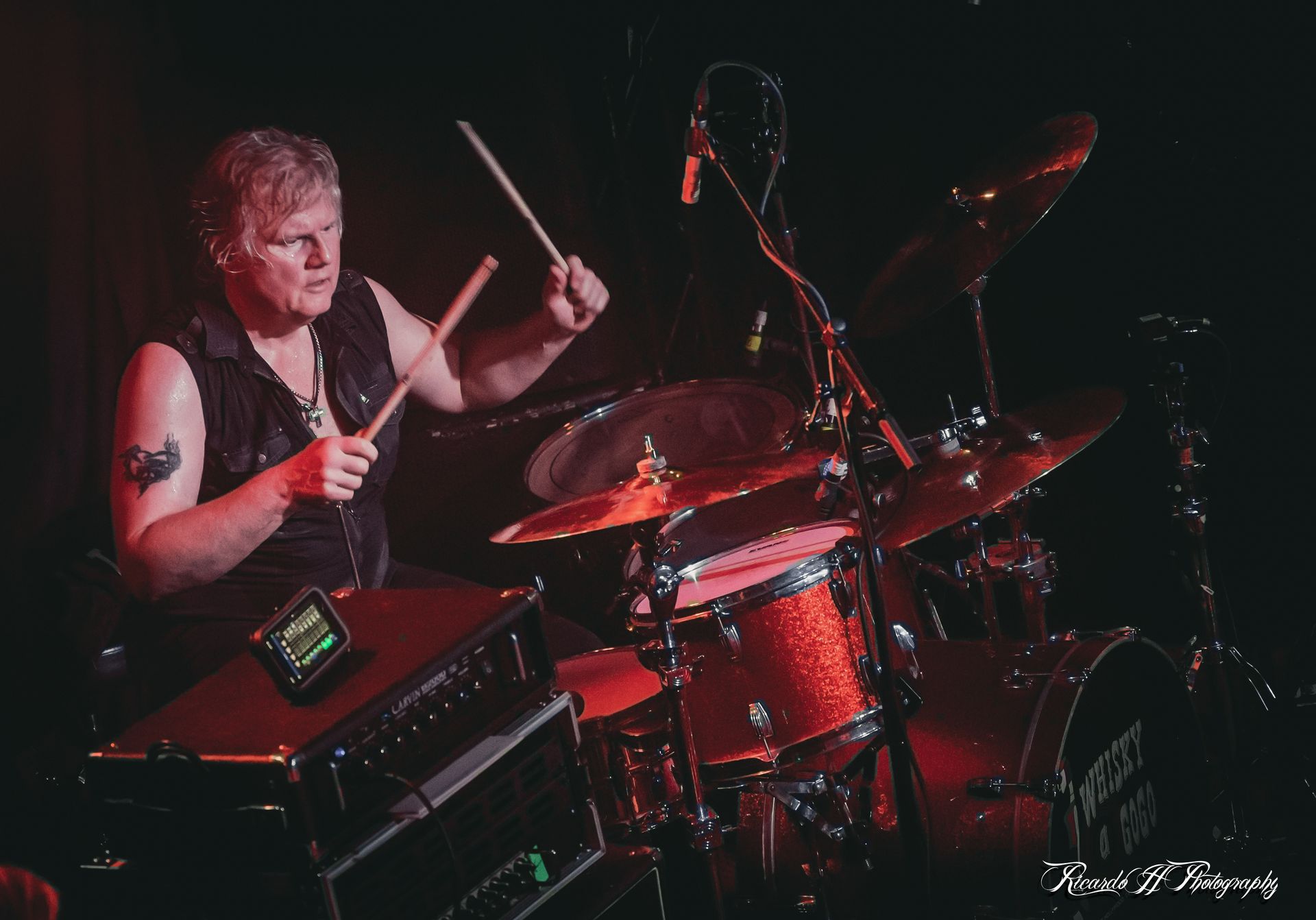 A man is playing drums on a stage in a dark room.