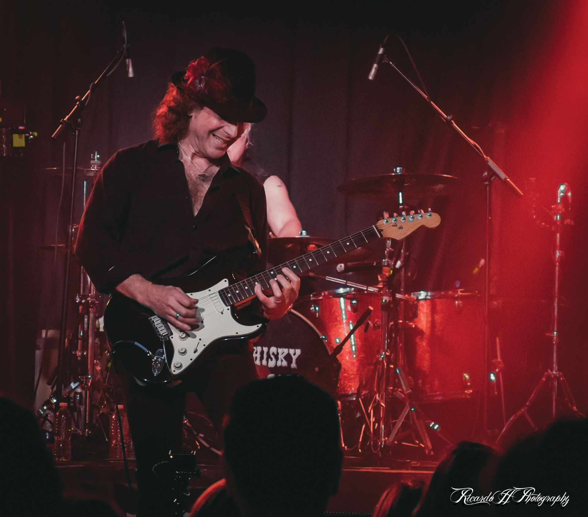 A man playing a guitar in front of a drum set that says jicky