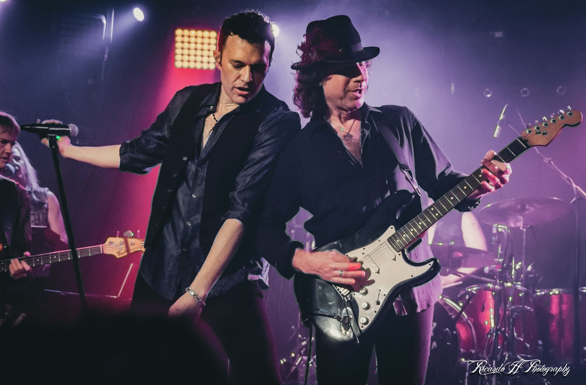 Two men are playing guitars and singing into microphones on a stage.