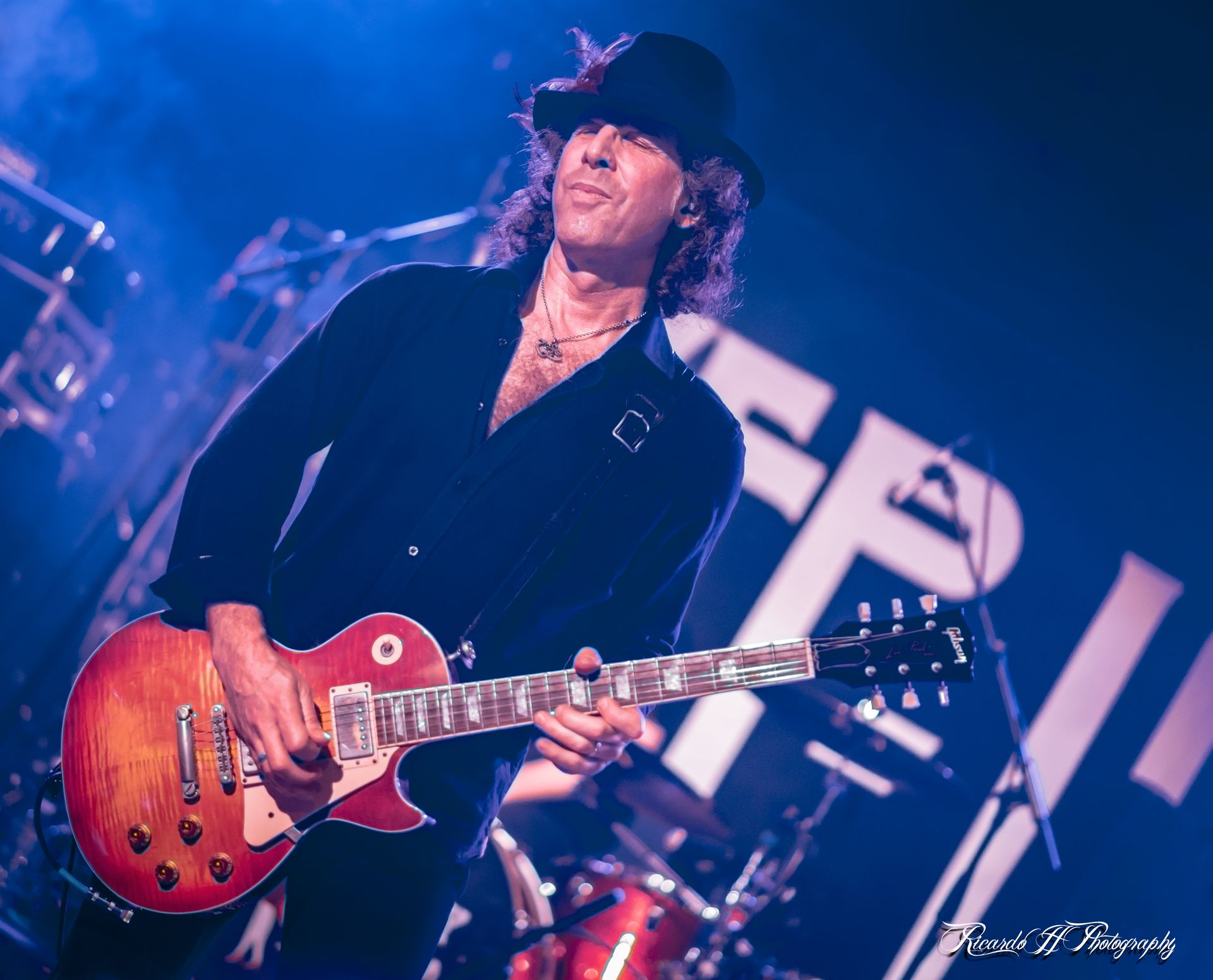 A man in a hat is playing a guitar on a stage.