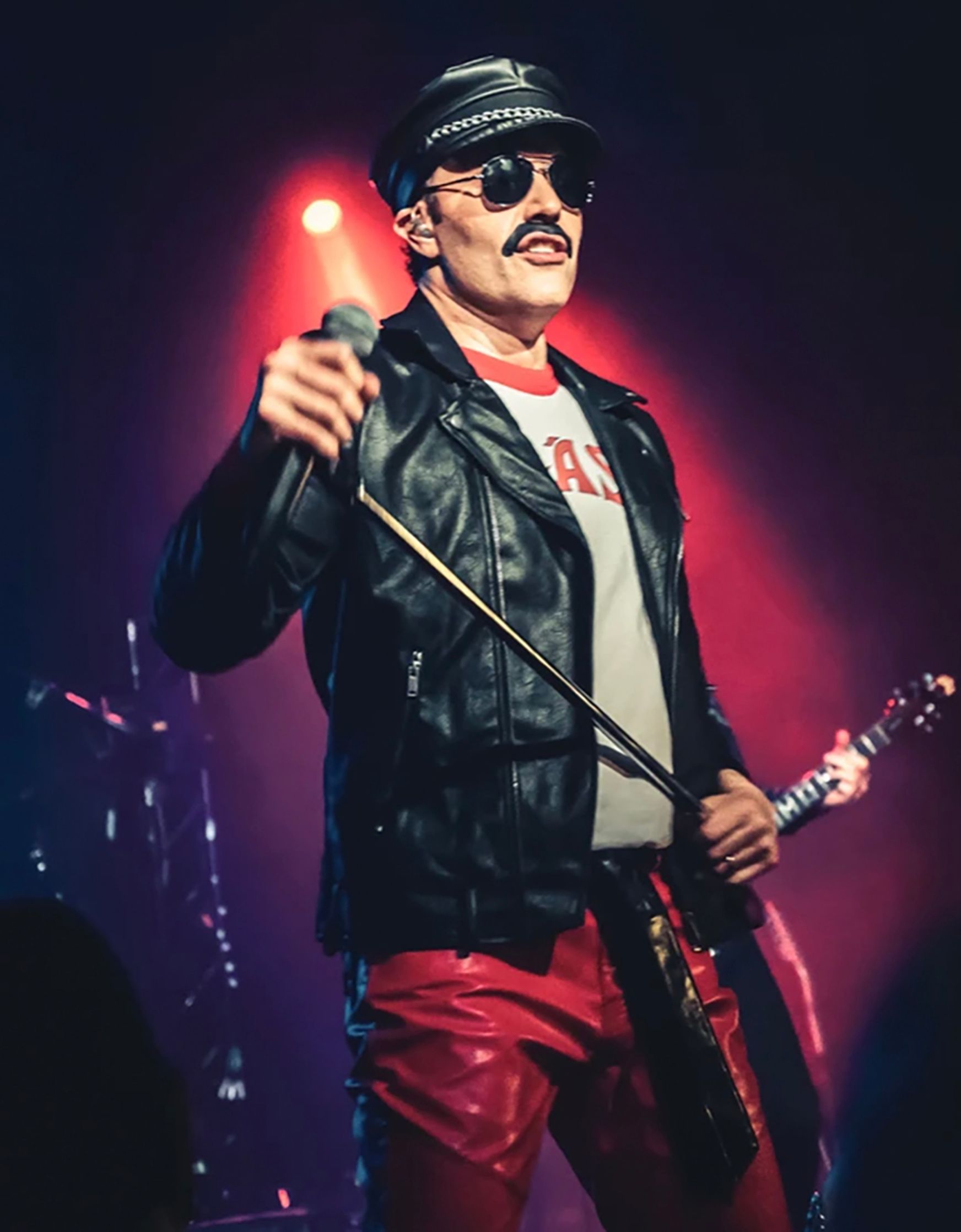 A man with a mustache is singing into a microphone while holding a guitar.