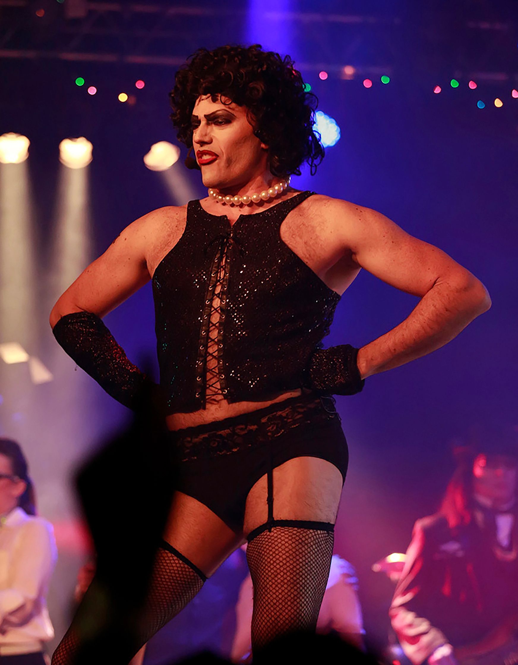 A man dressed as a woman is standing on a stage with his hands on his hips