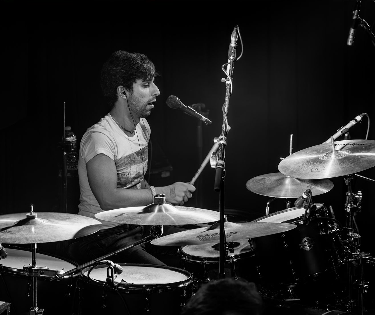A man is playing drums in front of a microphone in a black and white photo.
