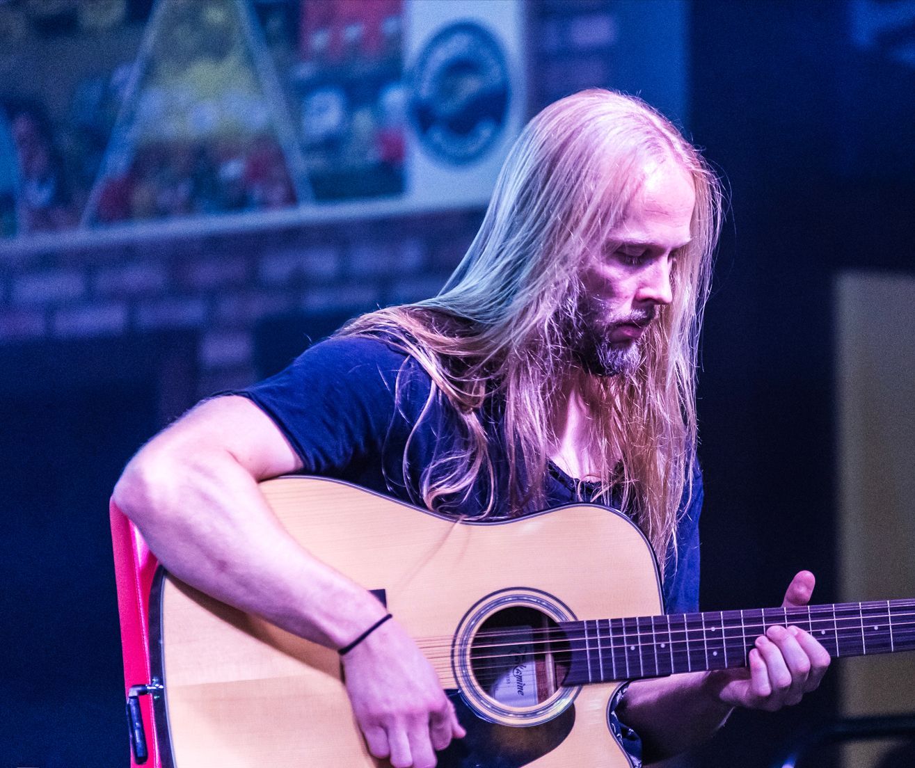 A man with long hair is playing an acoustic guitar on a stage.