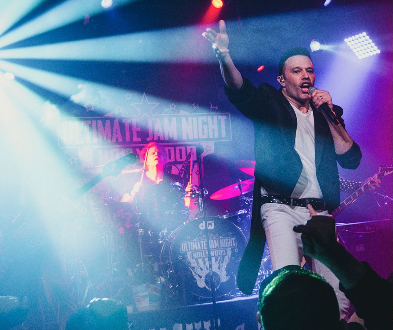A man is singing into a microphone on stage at a jam night