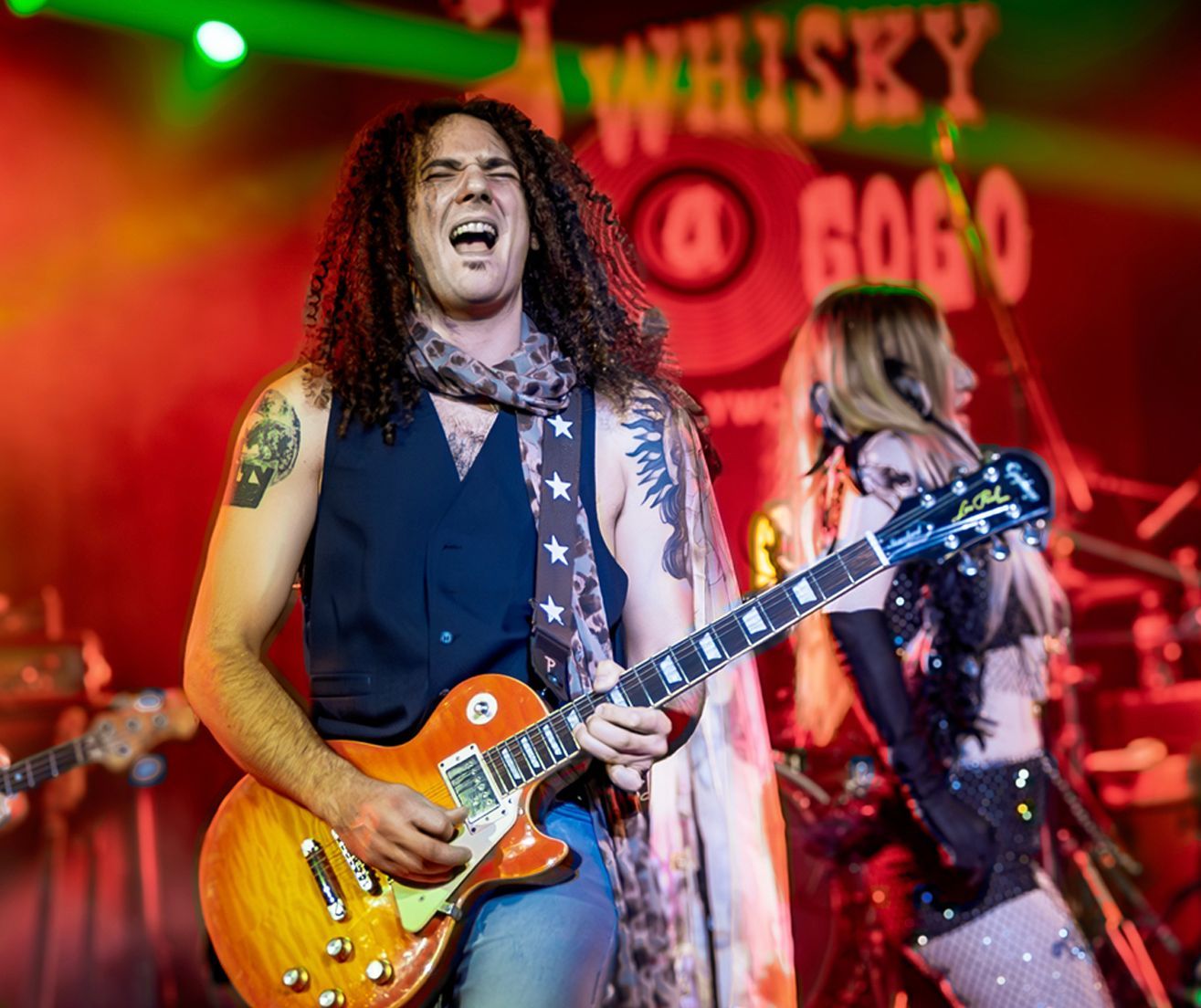 A man with long hair is playing a guitar on a stage.