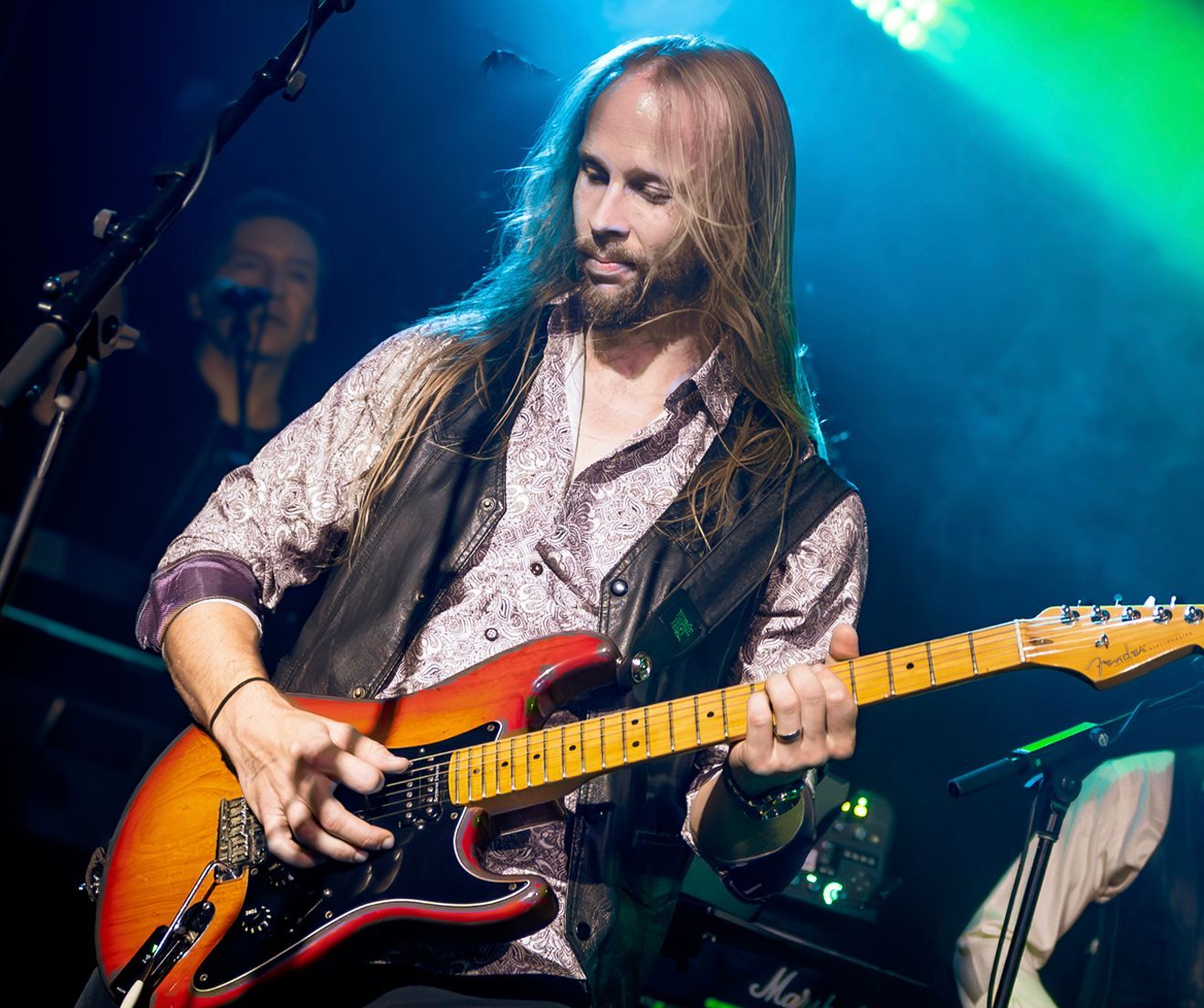 A man with long hair is playing a guitar on stage